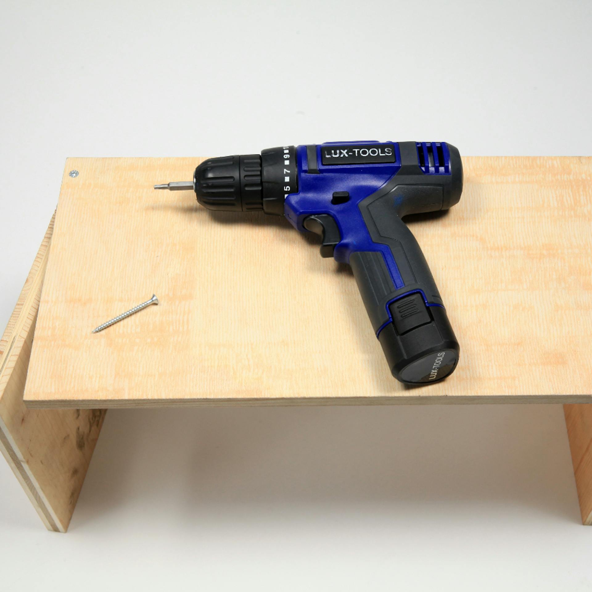 Akkuschrauber und Schraube liegen auf einer fast zusammengebauten Box aus Holzbrettern.
