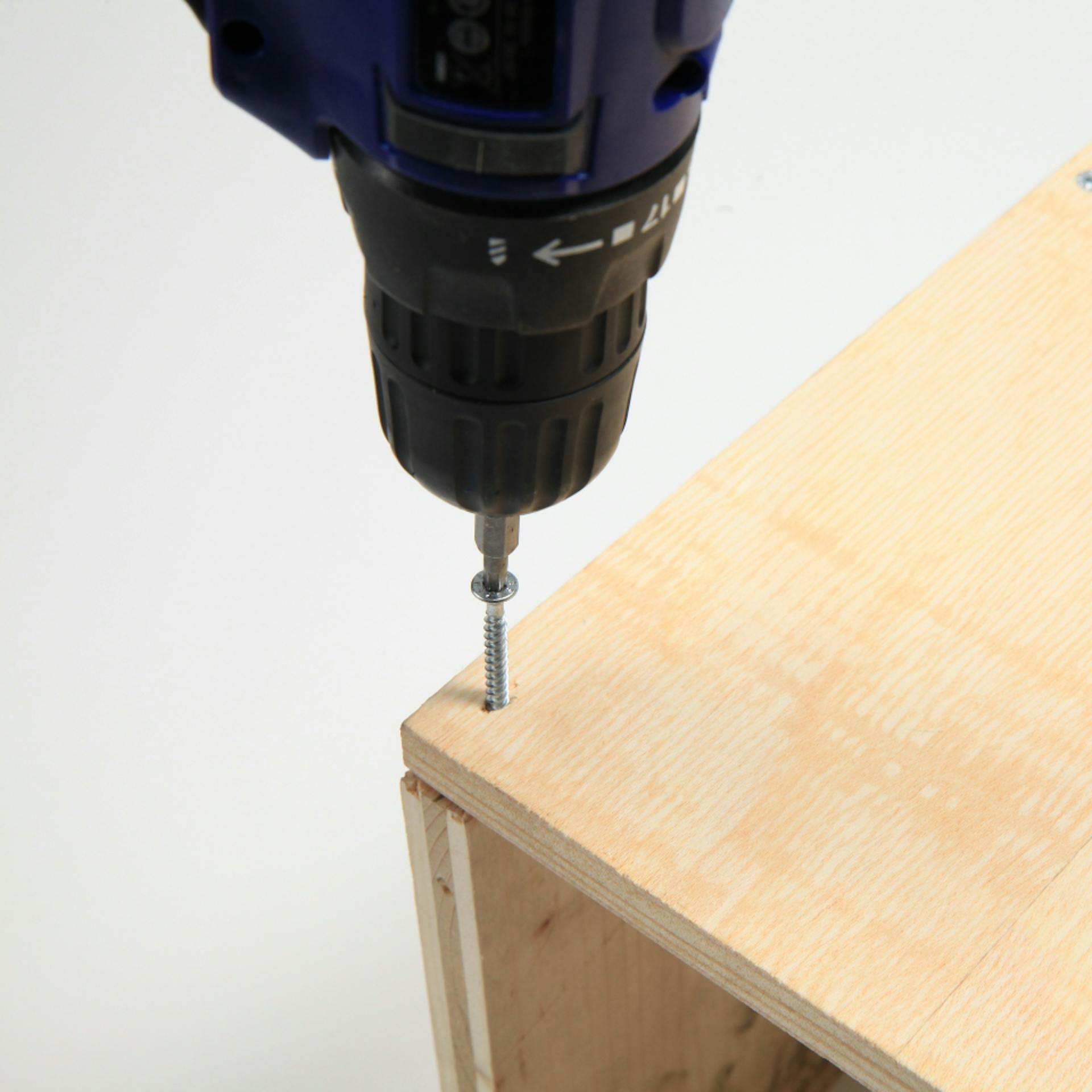 Person bohrt Schraube mit Akkuschrauber in Seitenwand einer Holzkiste