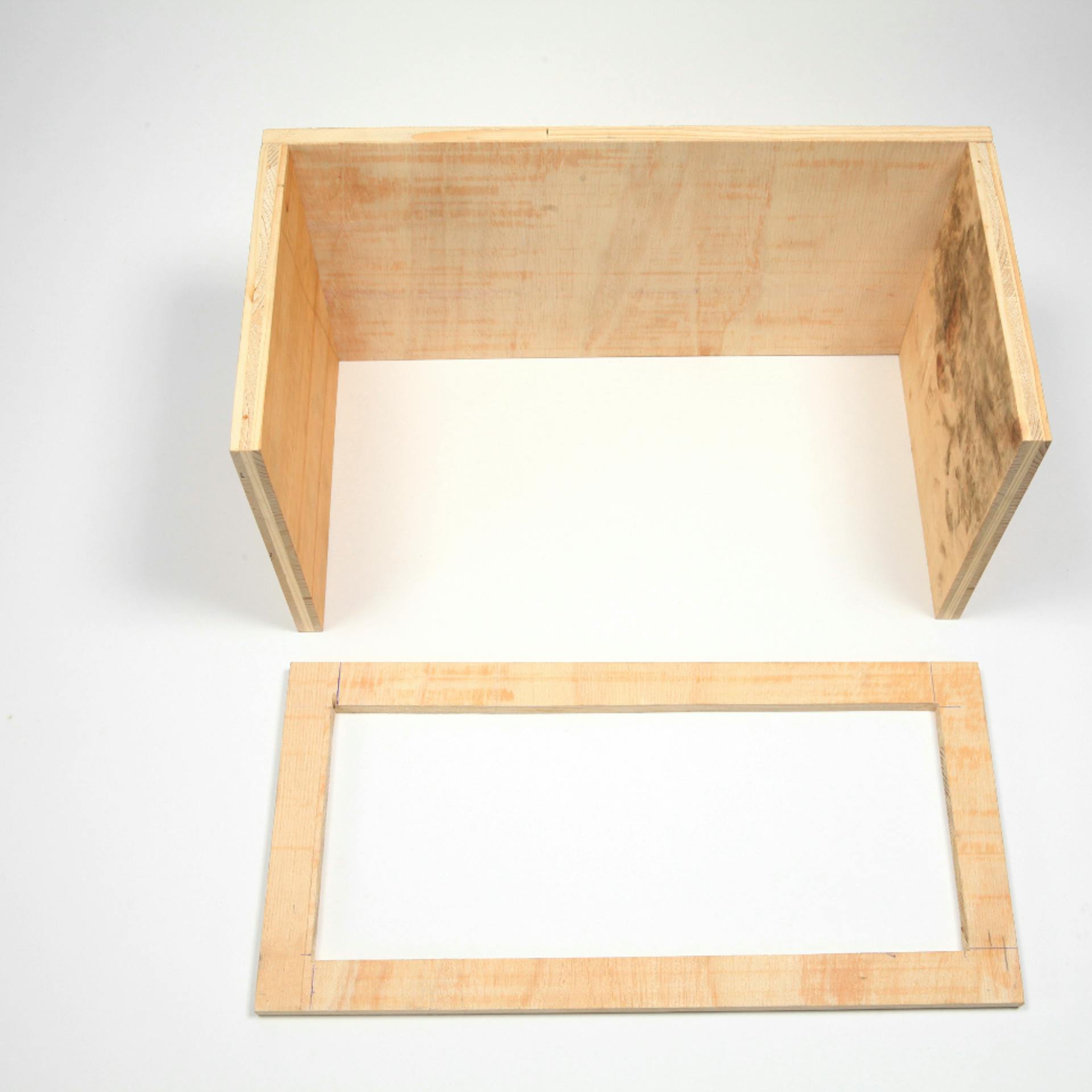 Rahmen aus Holz liegt neben zusammengebauter Rückwand und Seitenteile für Zauberschachtel