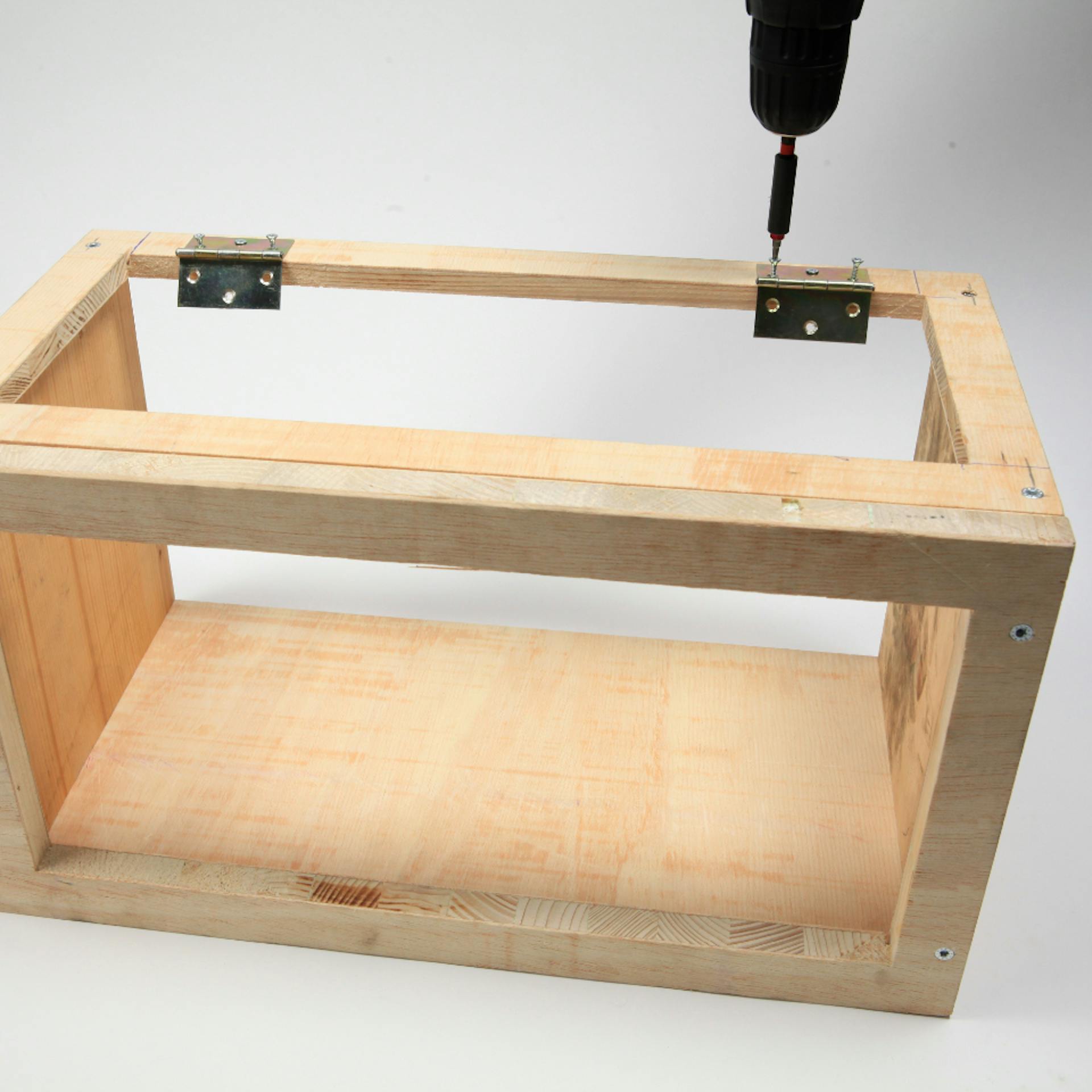 Person schraubt Scharniere mit Akkuschrauber an fast fertiger Box an.