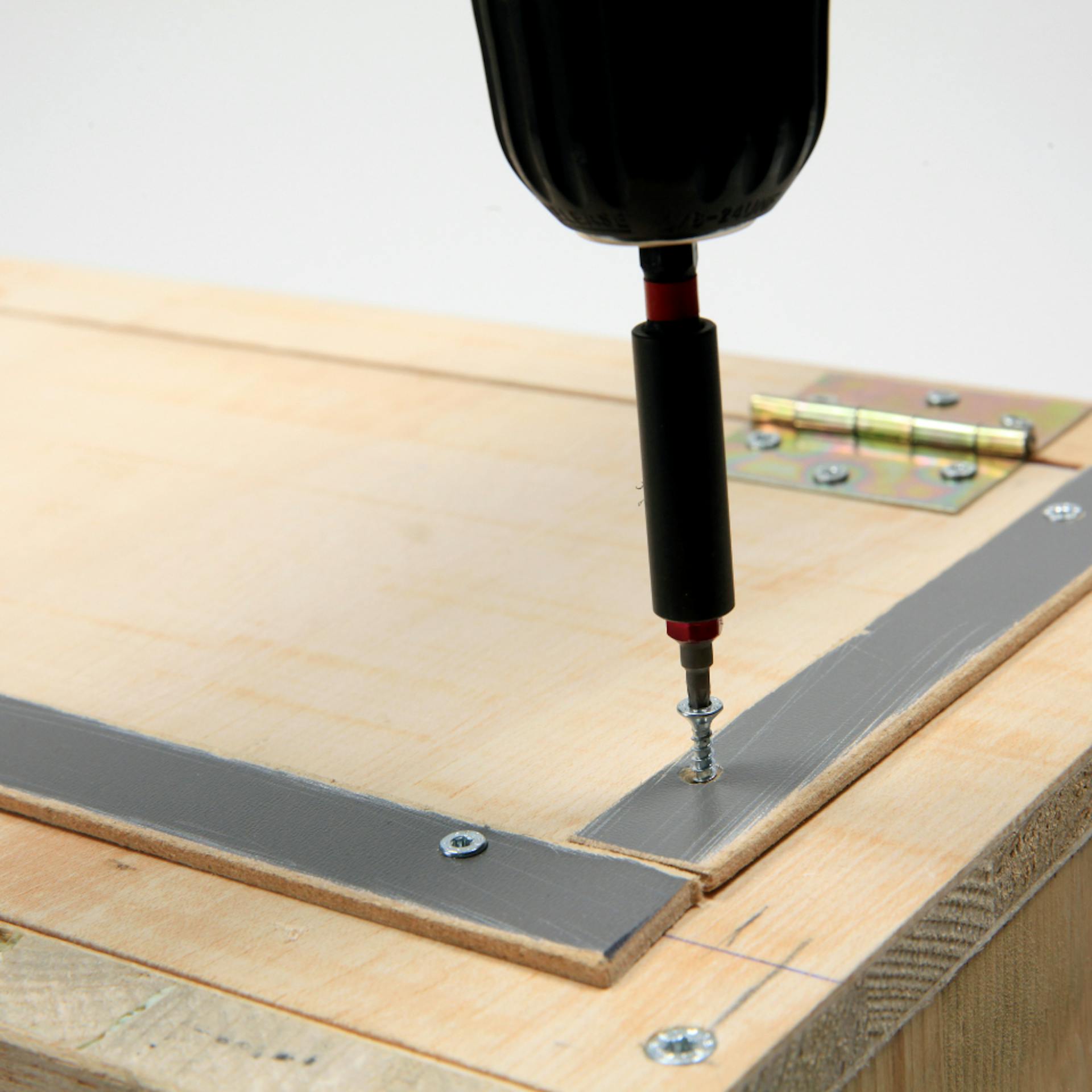 Person schraubt mit Akkuschrauber dünne Leisten an Tür einer Holzbox.