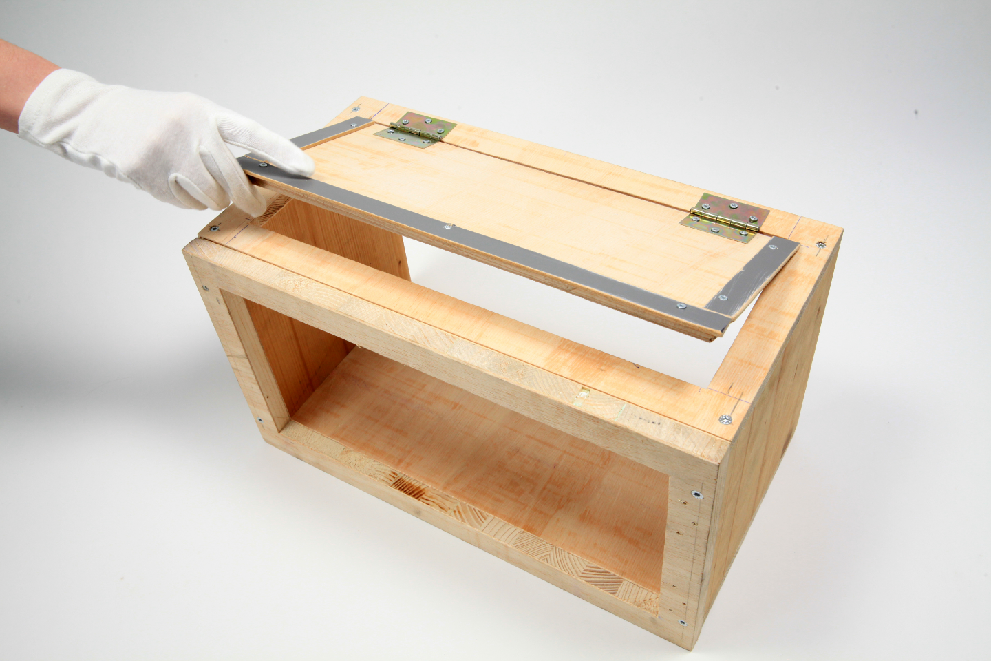 Person öffnet mit weißem Stoffhandschuh Deckel einer fast fertigen Box aus Holz.
