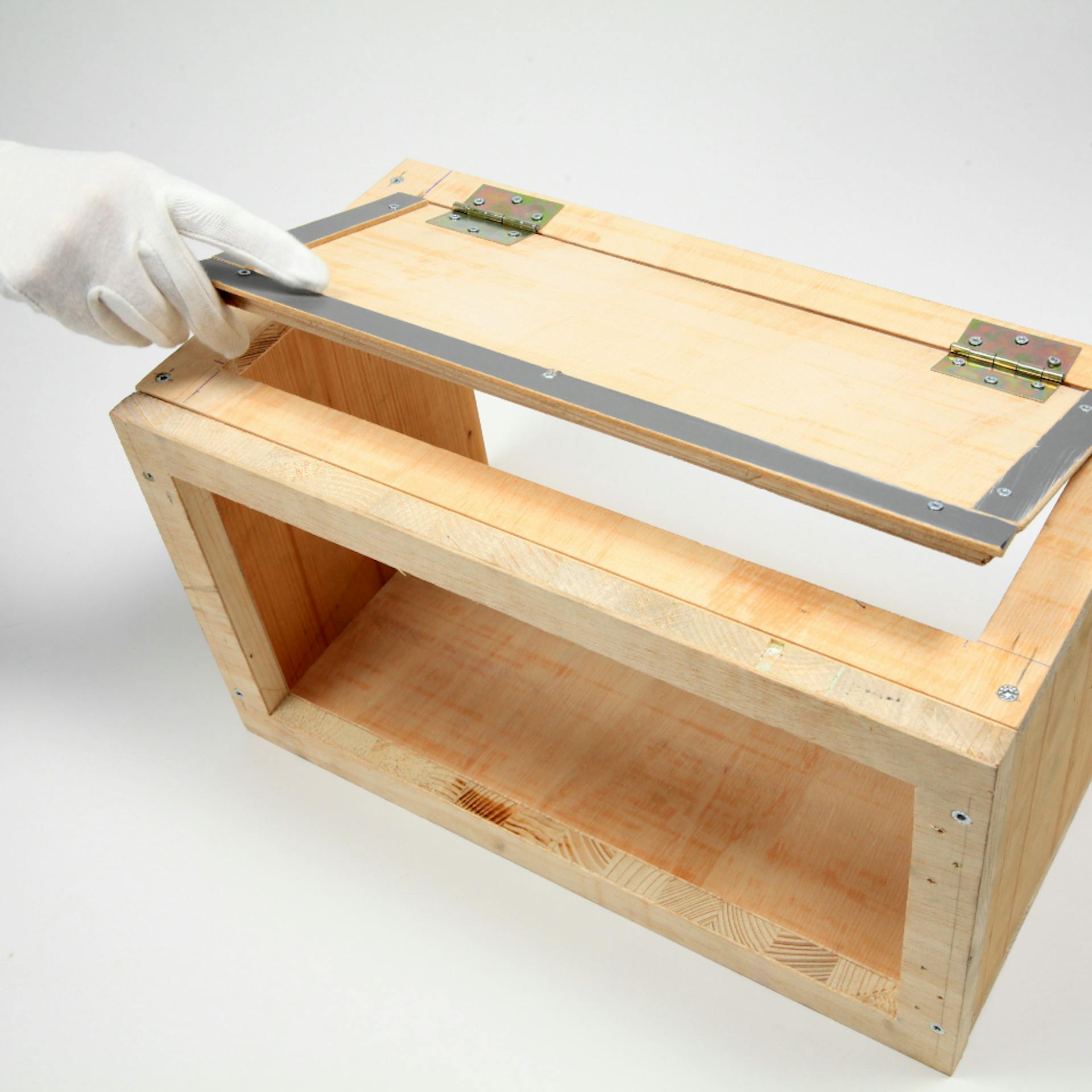Person öffnet mit weißem Stoffhandschuh Deckel einer fast fertigen Box aus Holz.
