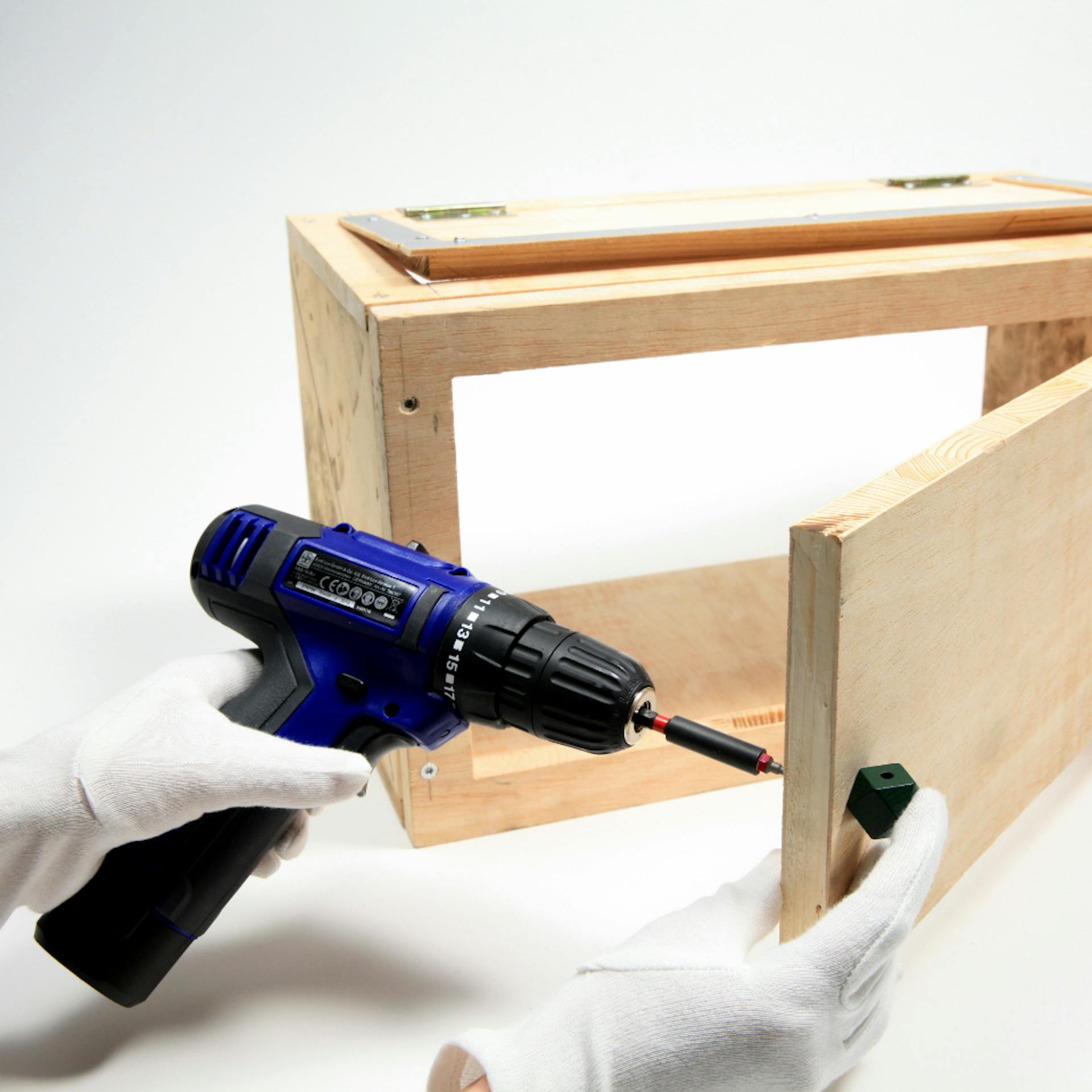 Person schraubt mit weißen Stoffhandschuhen und Akkuschrauber Zierknauf an geöffneter Tür von Box fest.