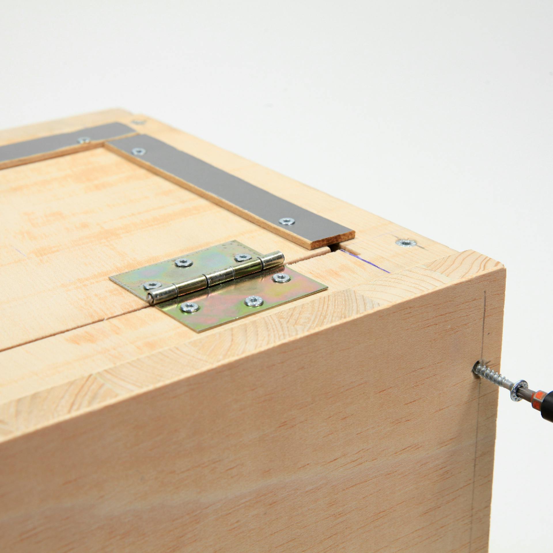 Person schraubt Rückseite von Holzbox mit Akkuschrauber und Schrauben fest.