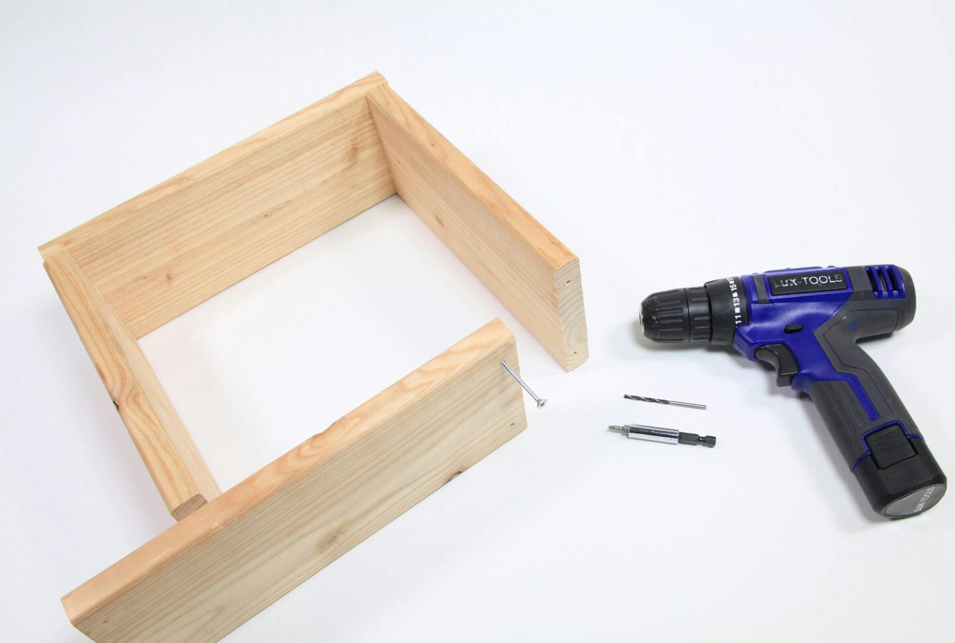 Egy fakeret látható, amelynek az egyik oldala még nincs összecsavarozva. Mellette egy akkus csavarozó különböző tartozékokkal