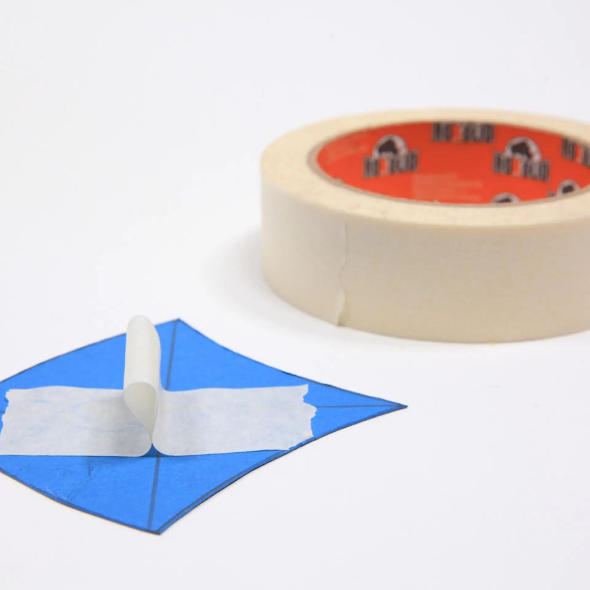 Es ist ein blaues Stück Papier in Schuppenform zu sehen. Auf der Form ist ein Stück Kreppband befestigt. Im Hintergrund liegt eine Rolle Kreppband.