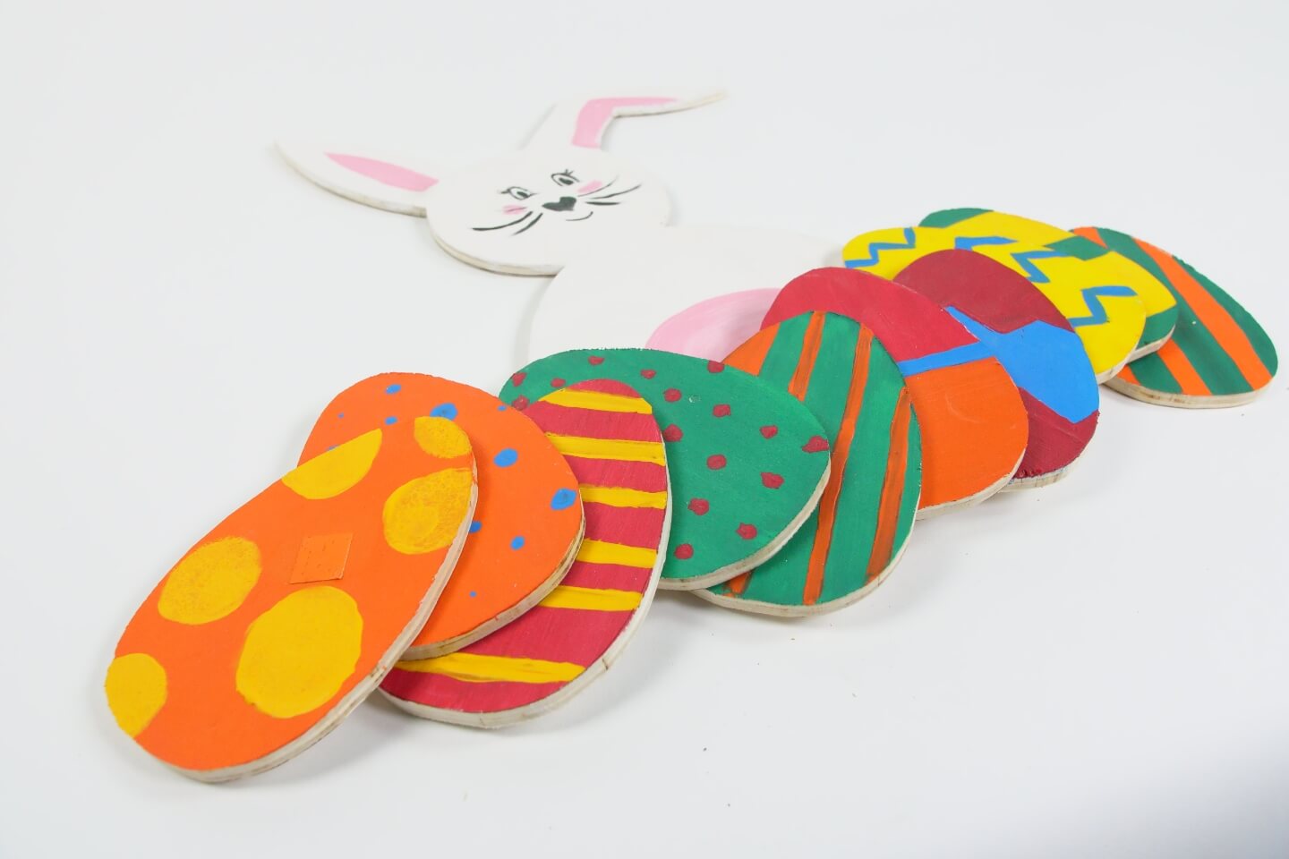 Zajačik a farebne maľované drevené veľkonočné vajíčka ležia na podklade