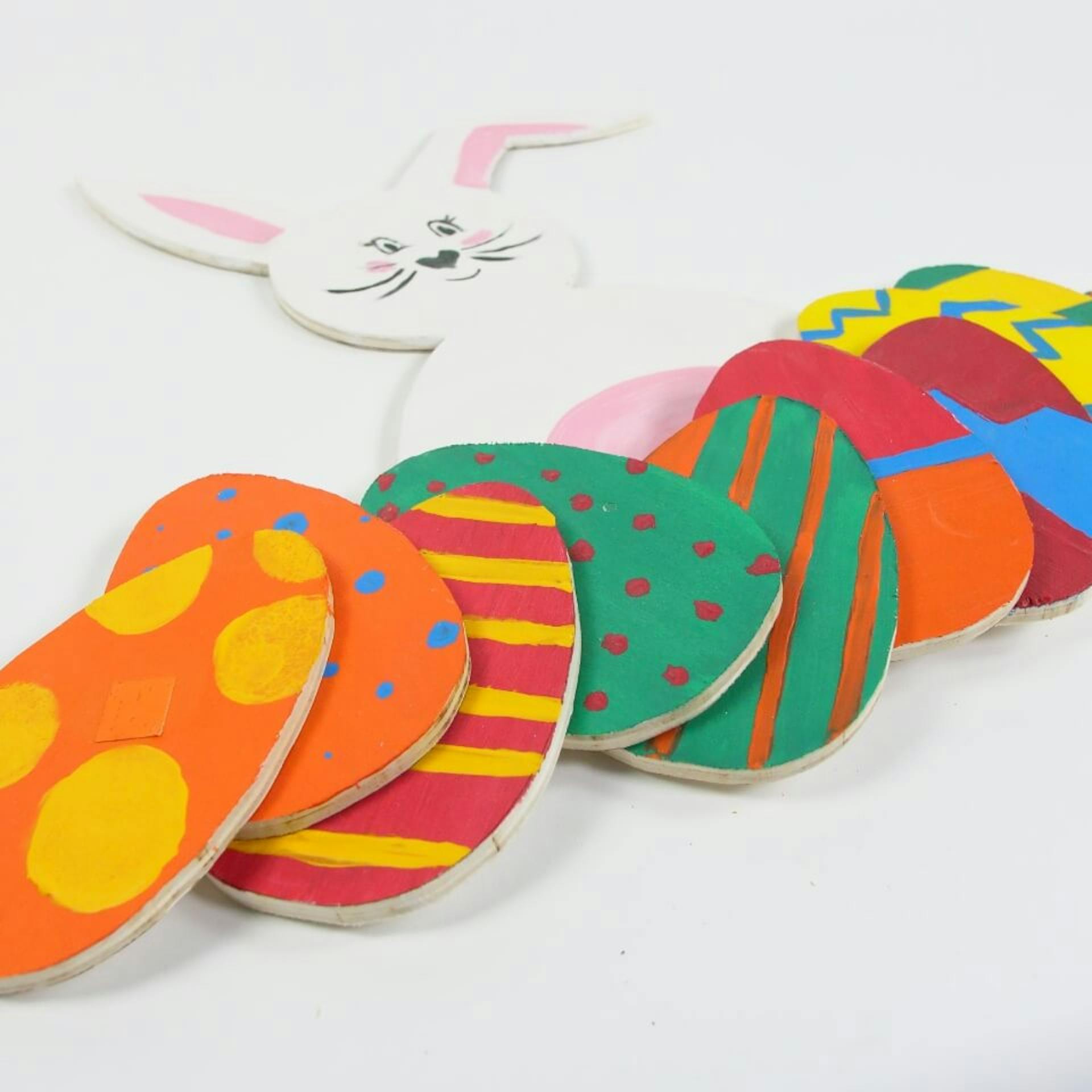 Zajačik a farebne maľované drevené veľkonočné vajíčka ležia na podklade