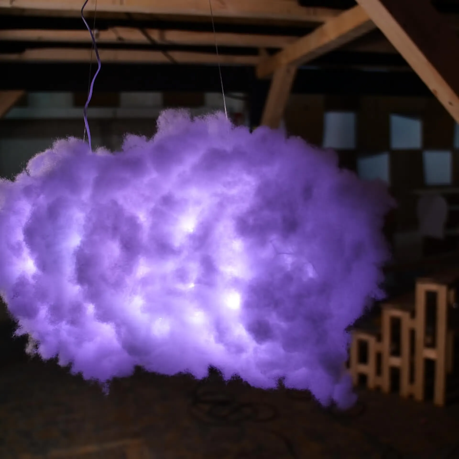 Lila leuchtende Wolkenlampe baumelt von einem Holzgestell herab.
