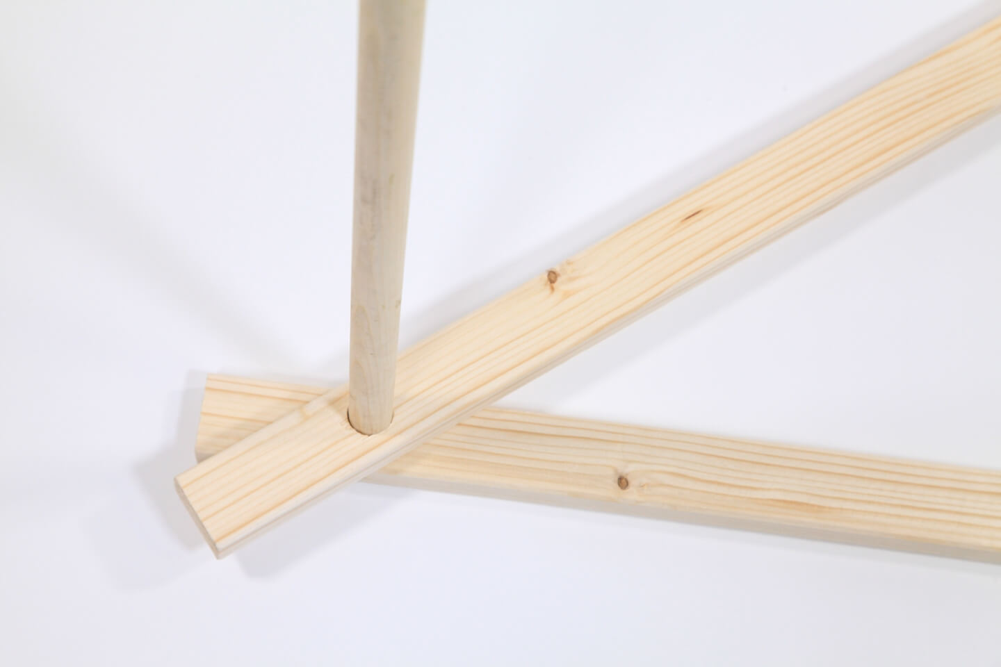 Su sfondo bianco, due travi sovrapposte alle estremità. I fori delle travi sono allineati e in essi è inserita una barra di legno che sporge verso l’alto.