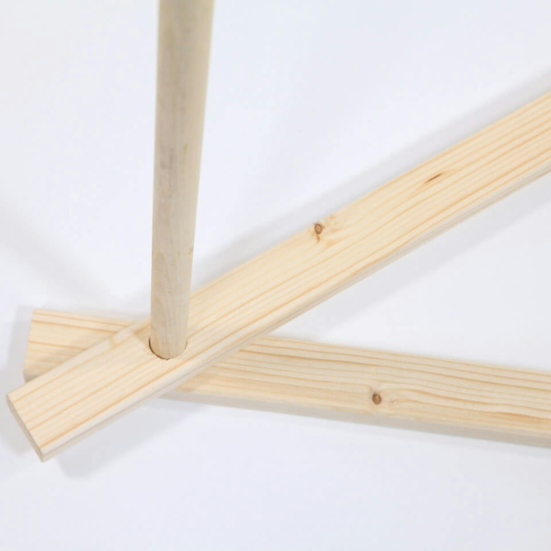 Auf einem weißen Untergrund liegen zwei Kanthölzer, deren Enden übereinander liegen. Die Löcher der Kanthölzer überlappen sich. In den Löchern steckt ein Holzstab und ragt in die Höhe.