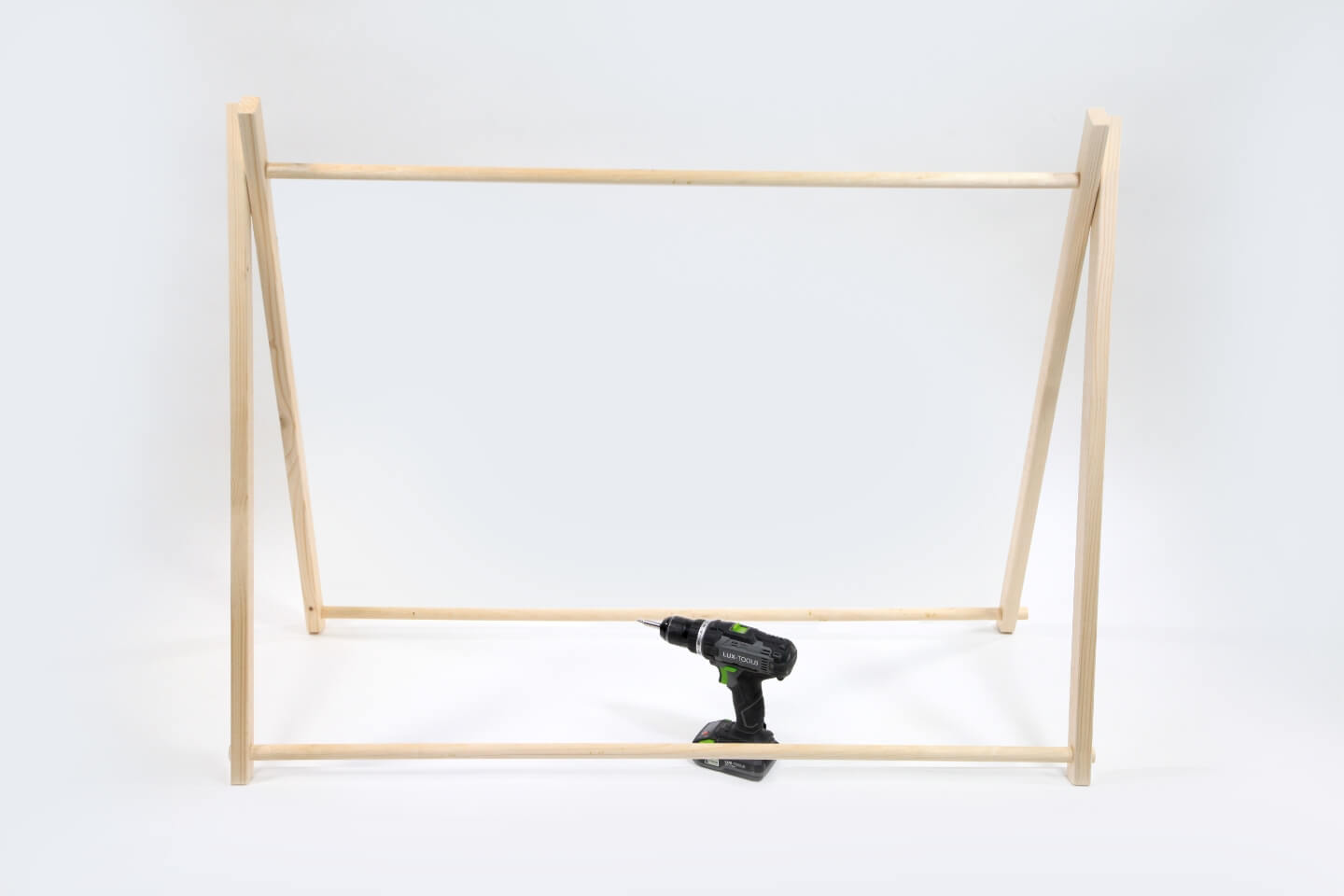 Telaio in legno di una tenda su sfondo bianco. Al centro del telaio si trova un avvitatore a batteria.