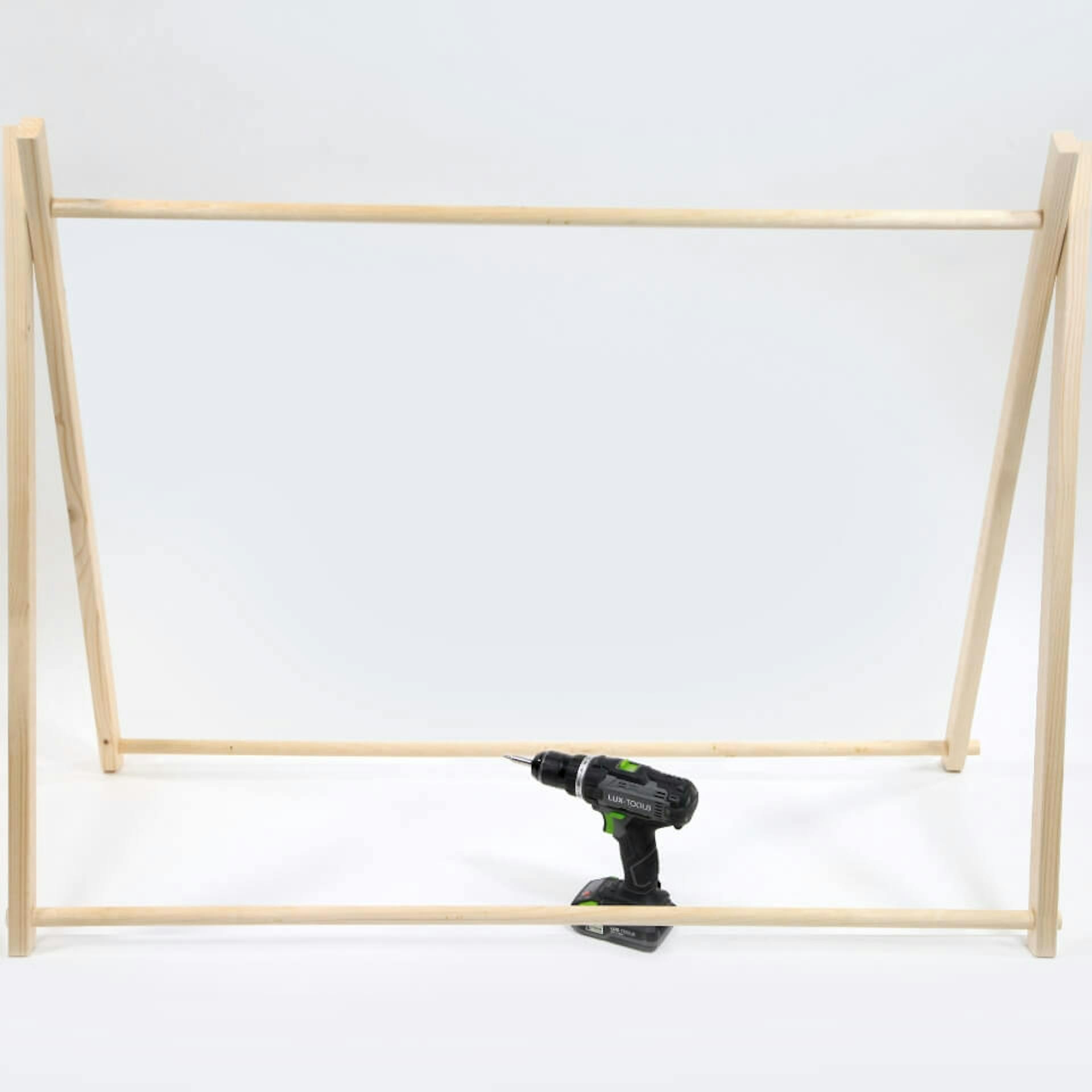 Vor einem weißen Hintergrund ist das Holzgerüst eines Zeltes zu sehen. In der Mitte des Zeltes steht ein Akkuschrauber.