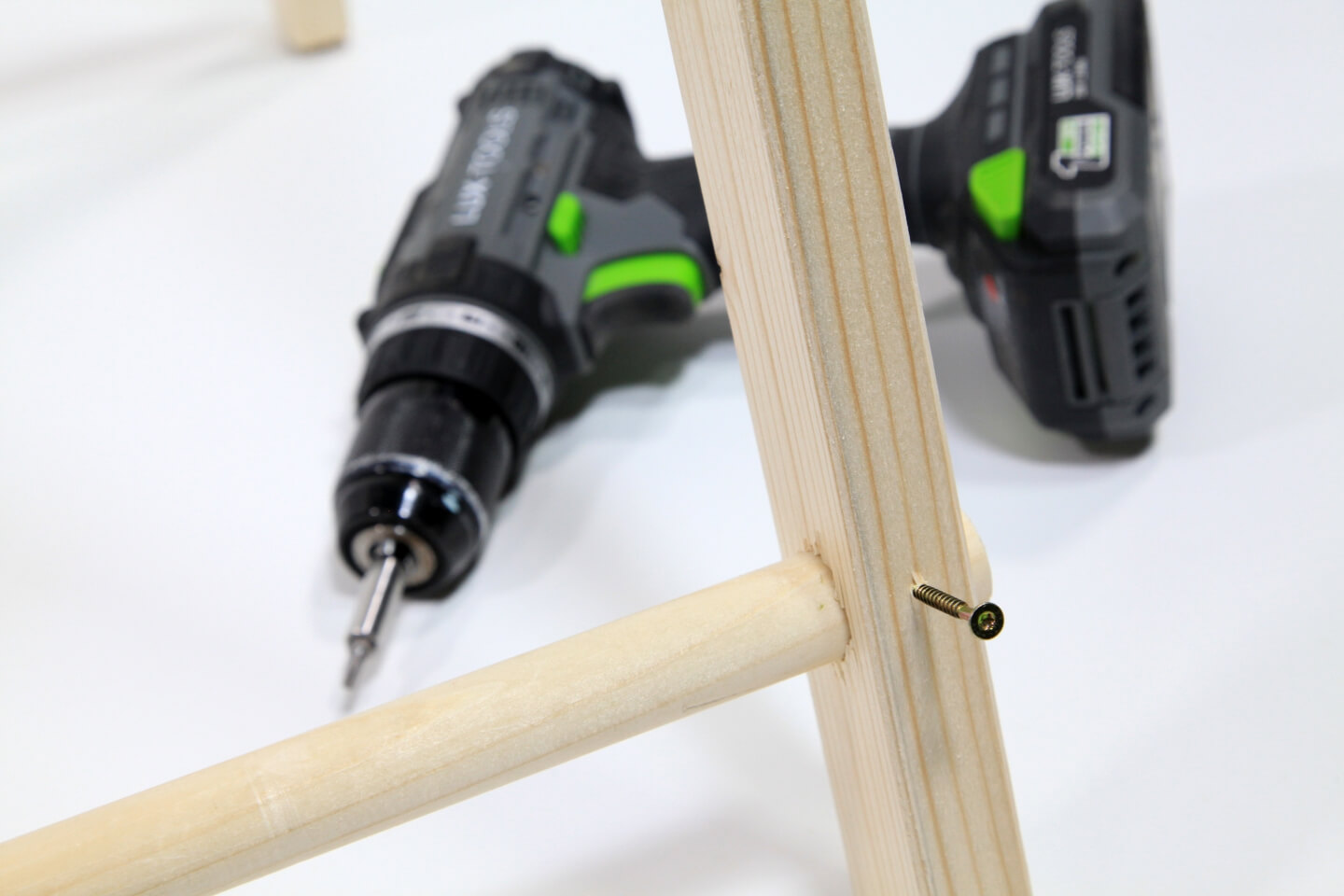 Base del telaio di legno di una tenda. Due elementi in legno sono collegati mediante una vite. Sullo sfondo è visibile un avvitatore a batteria.