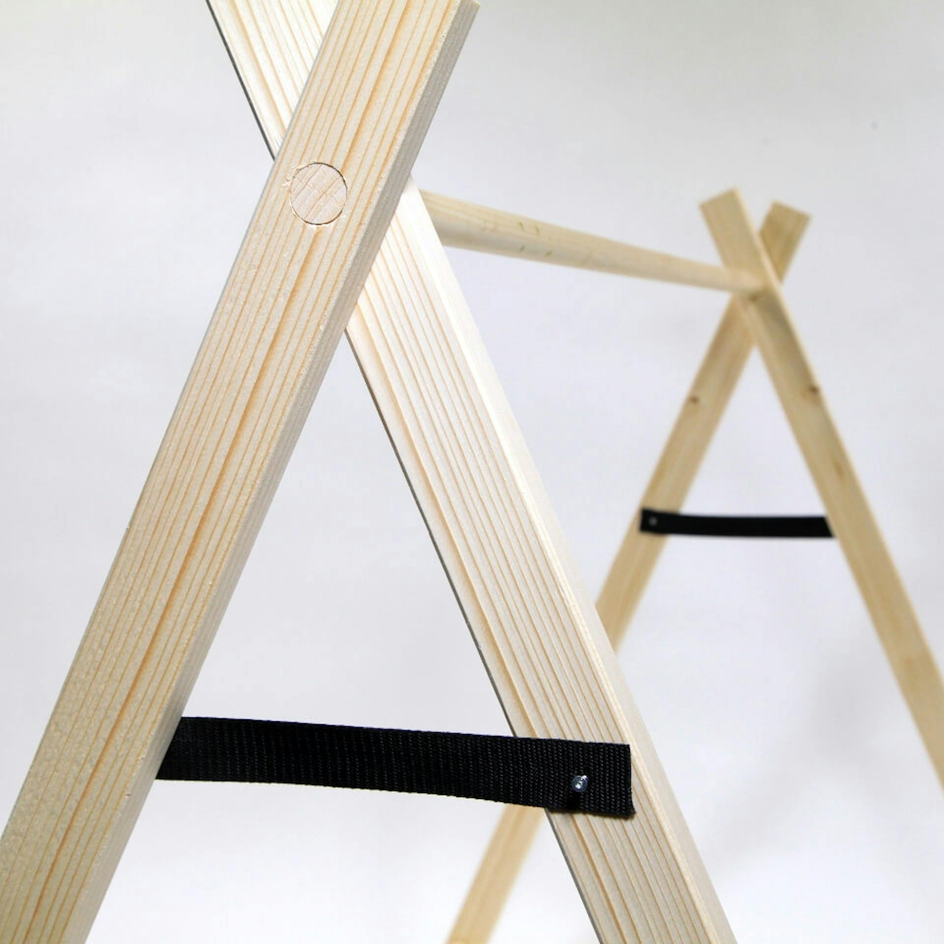 Es ist der Giebel eines Zeltes zu sehen. Die vorderen und hinteren Holzelemente sind jeweils durch ein schwarzes Textilband verbunden.