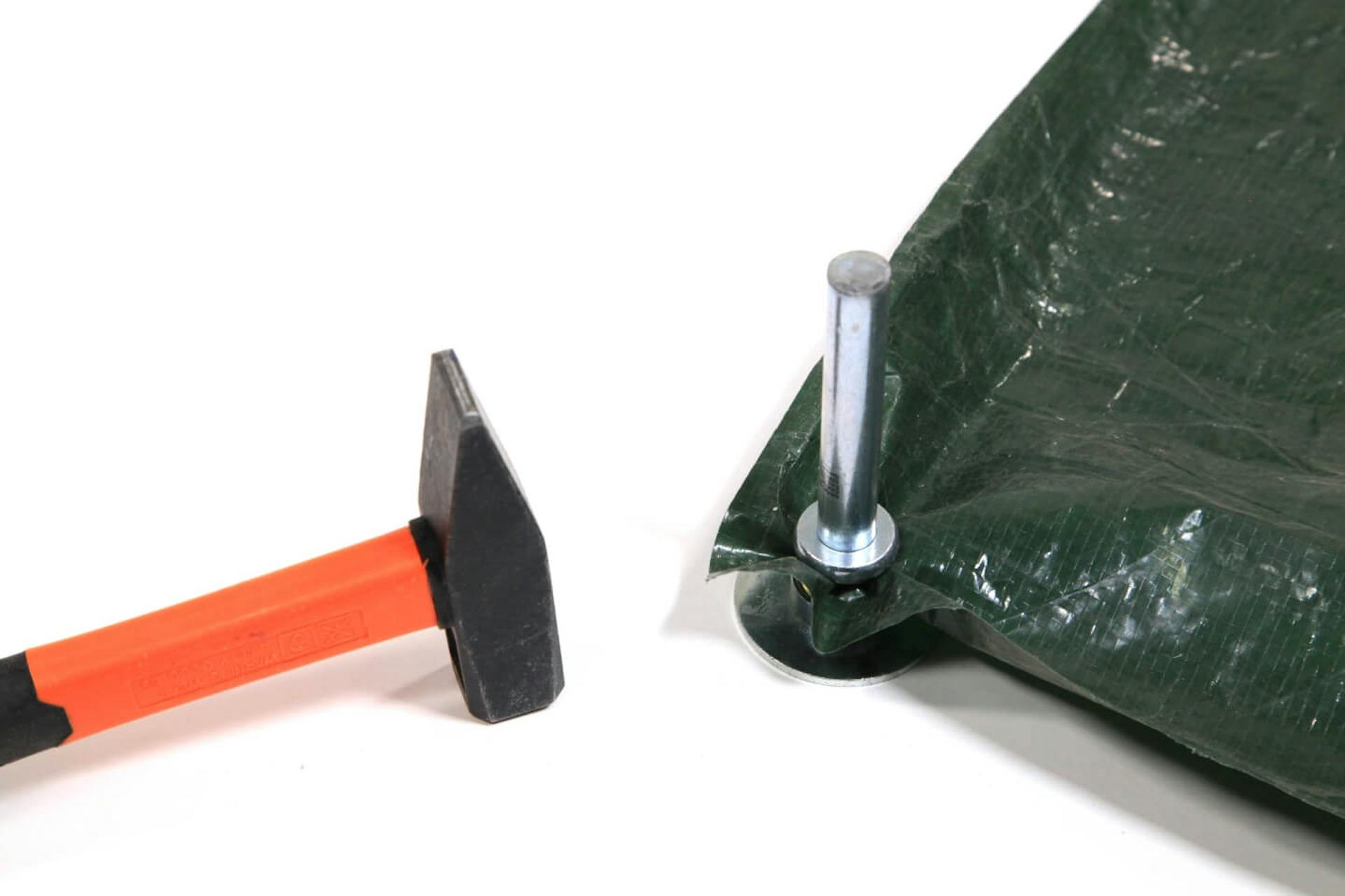 È visibile l’angolo di un telo scuro, al quale, con un attrezzo, viene fissato un occhiello. Accanto si trova un martello.