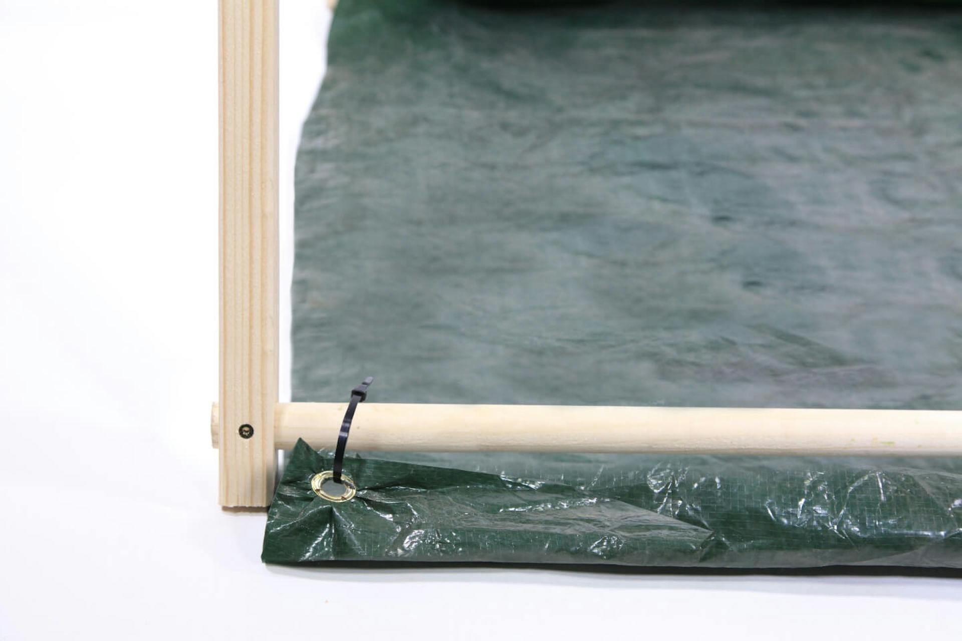 Due elementi di legno di una tenda collegati tra loro. A una barra è fissato un telo con l’ausilio di una fascetta serracavi.