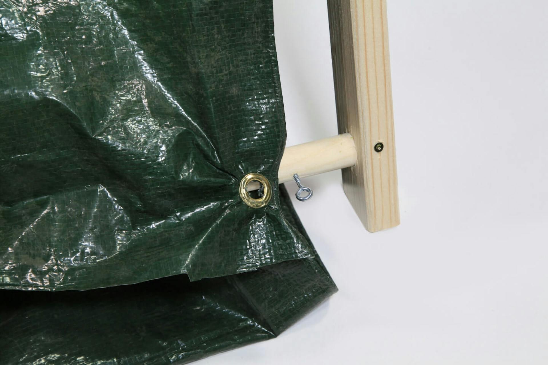 Base del telaio di legno della tenda su sfondo bianco. In una barra in legno è inserita una vite a occhiello. Sulla parte anteriore del telaio è fissato un telo scuro.