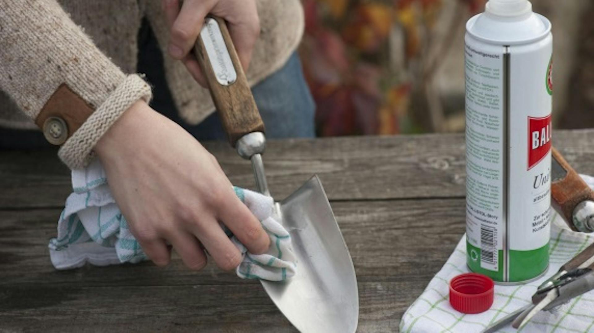 Jemand pflegt Metallteile einer Gartenschaufel mit einem Mittel zur Metallpflege.