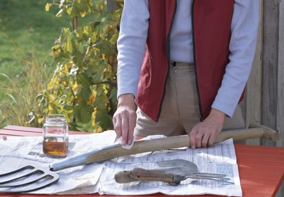 Jemand pflegt mit Pflegemittel den Stiel einer Grabegabel.