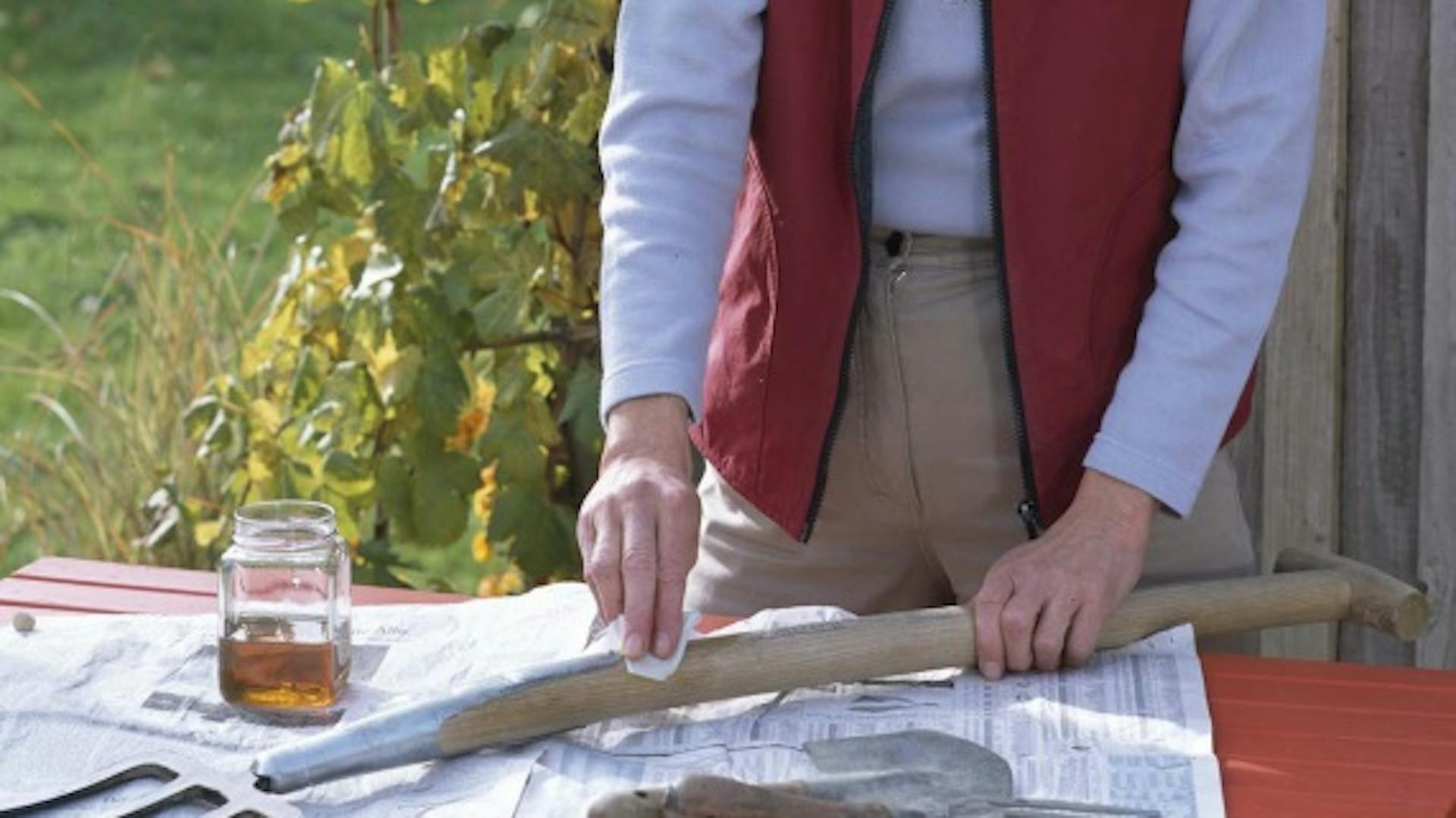 Jemand pflegt mit Pflegemittel den Stiel einer Grabegabel.