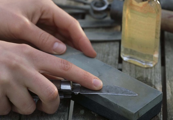 Jemand schärft ein Messer mit einem Schleifstein.