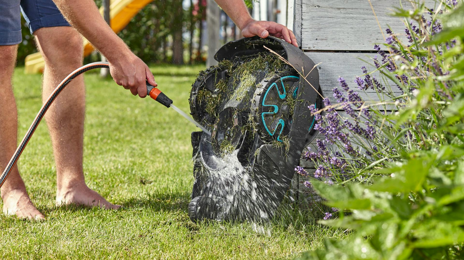 Mähroboter wird mit Gartenschlauch gesäubert