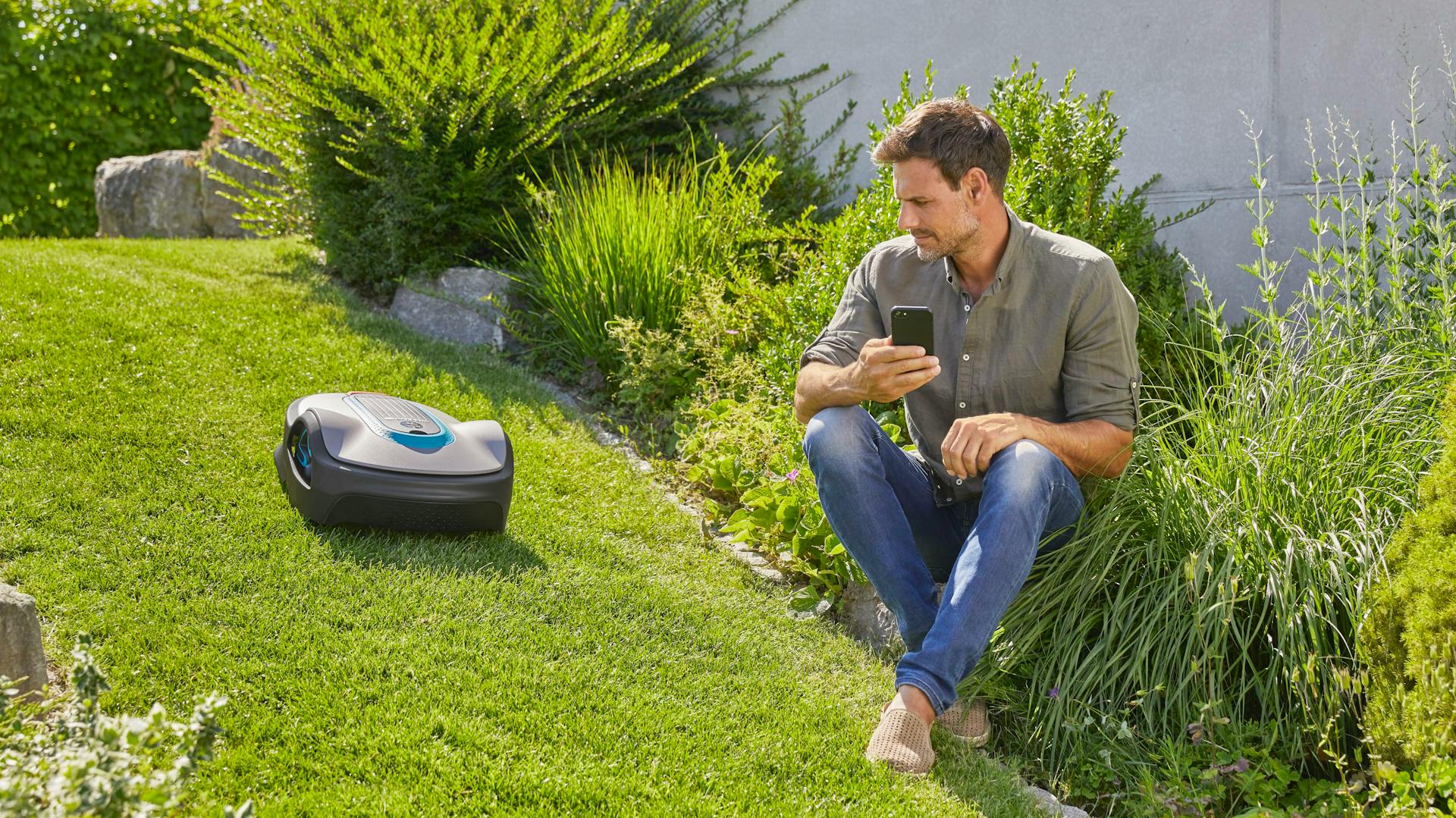 Mann steuert Mähroboter mit Handy