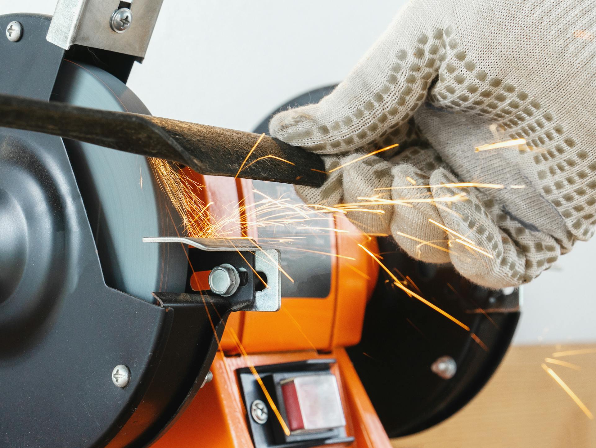 Jemand schleift das Messer eines Rasenmähers mit einer elektrischen Schleifmaschine.