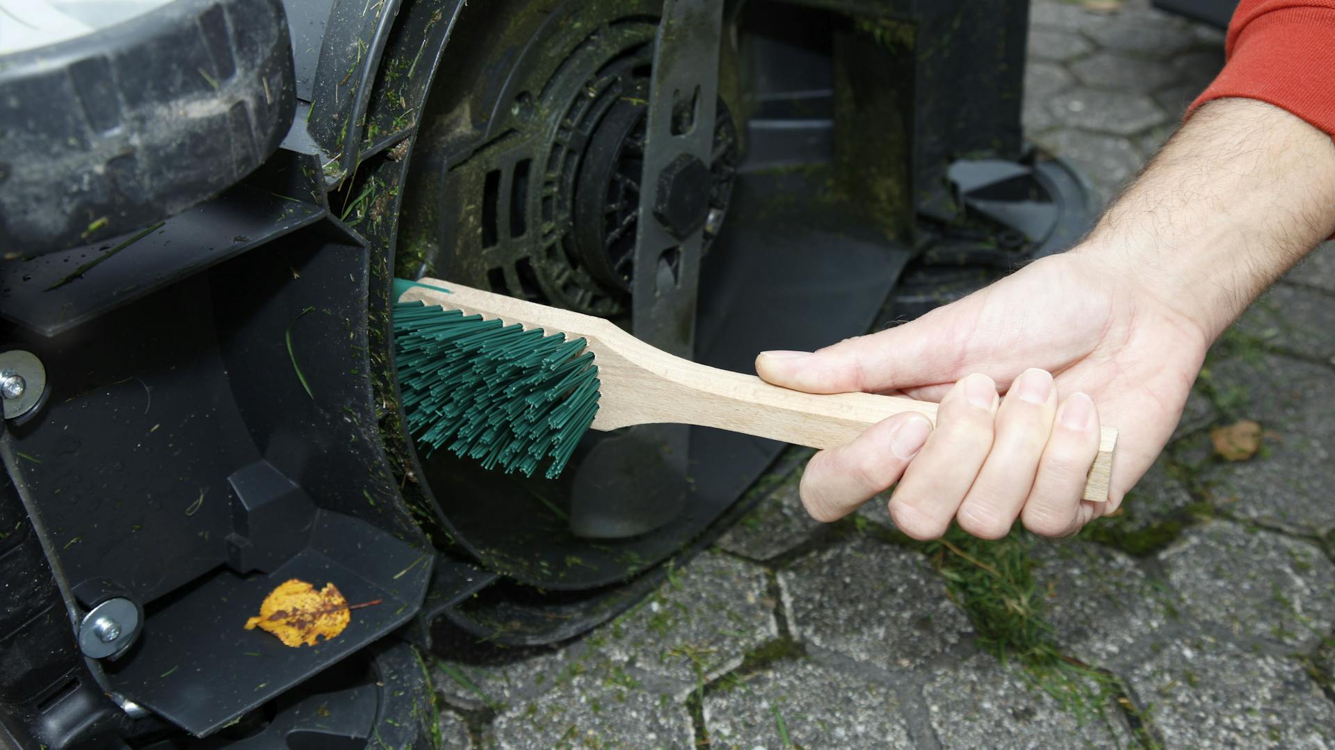 Jemand reinigt einen Rasenmäher mit einer Bürste.