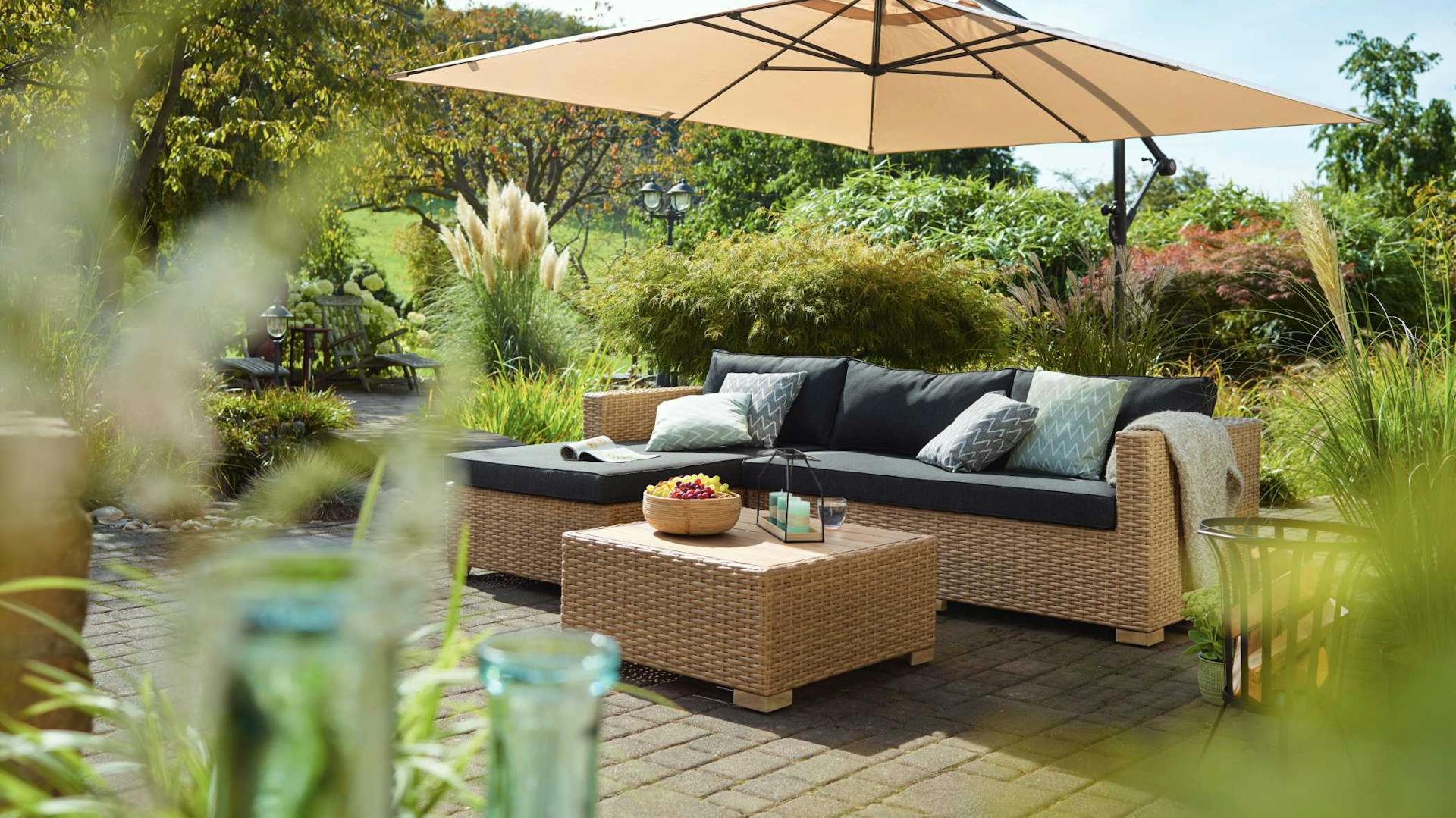 Gartengestaltung Loungegruppe auf Holzterrasse unter Sonnenschutz in üppig bepflanztem Garten
