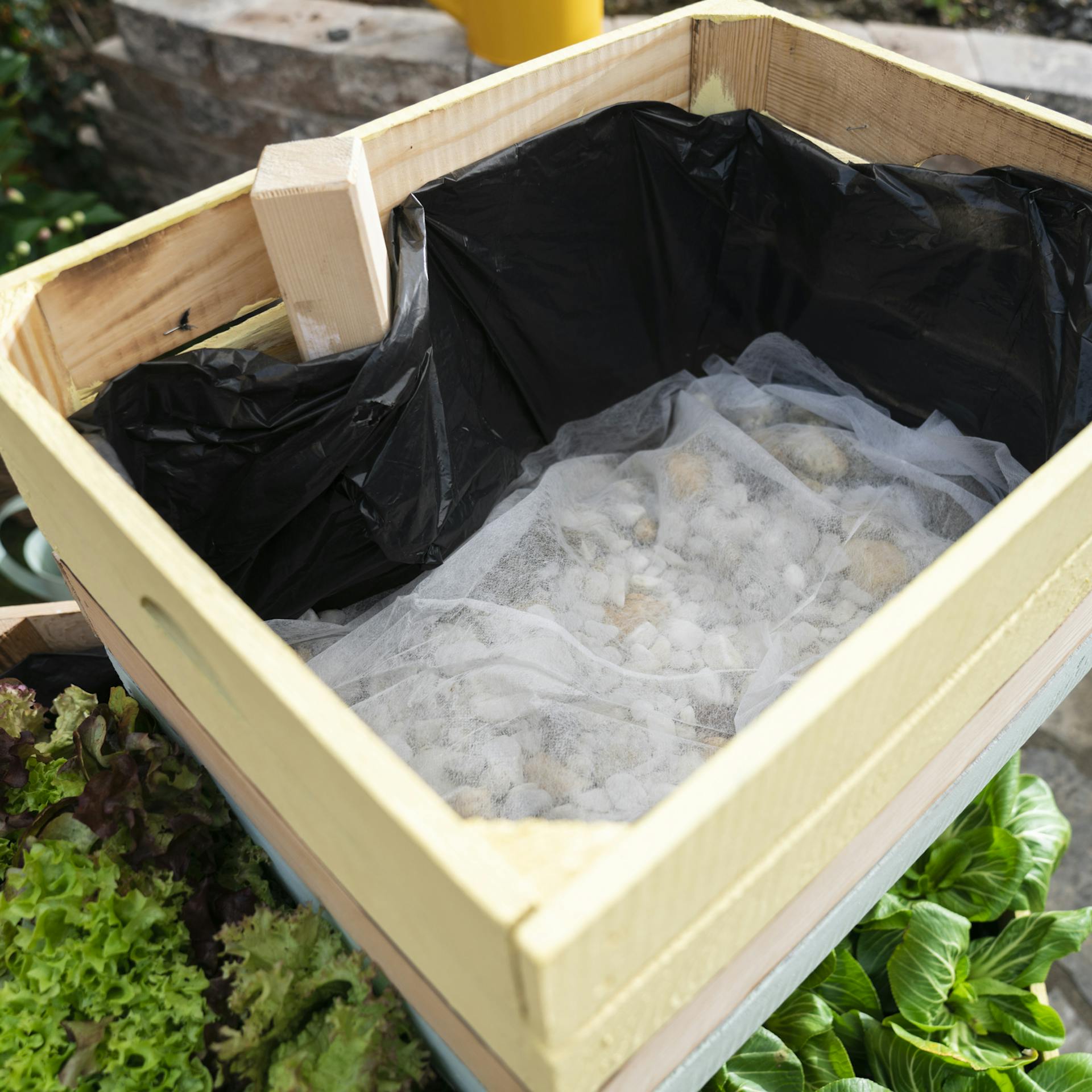 Die offene Holzkiste zeigt eine mit Vlies abgedeckte Schicht aus Kies.