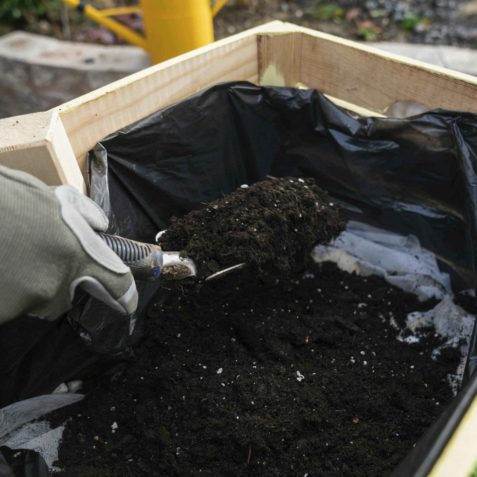 Eine Handvoll Kieselsteine wird über die noch nicht befüllte Holzkiste gehalten.