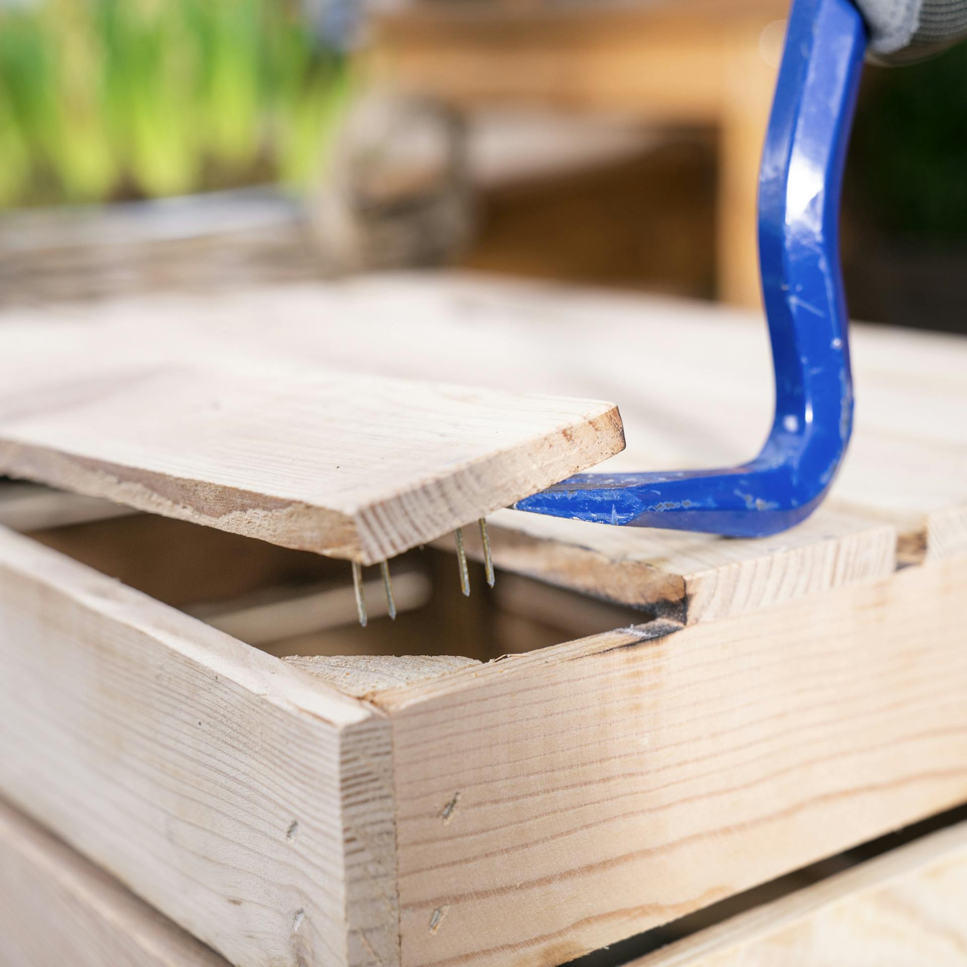 Nahaufnahme einer Holzkiste, an der ein Brecheisen angesetzt wird.