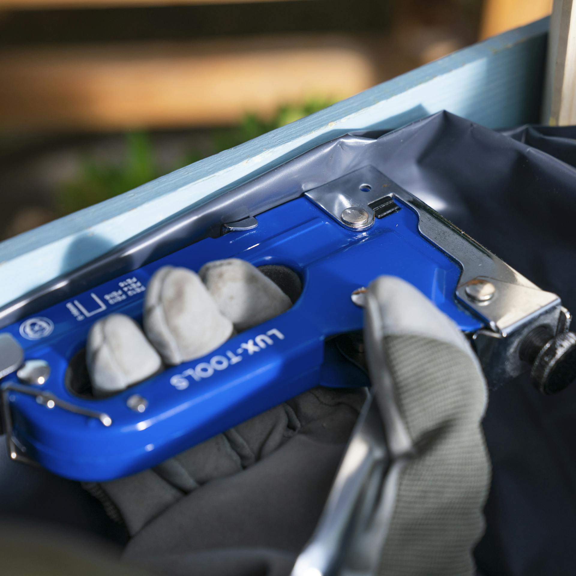 Dunkle Folie wird in die Innenseite einer blauen Holzkiste getackert.