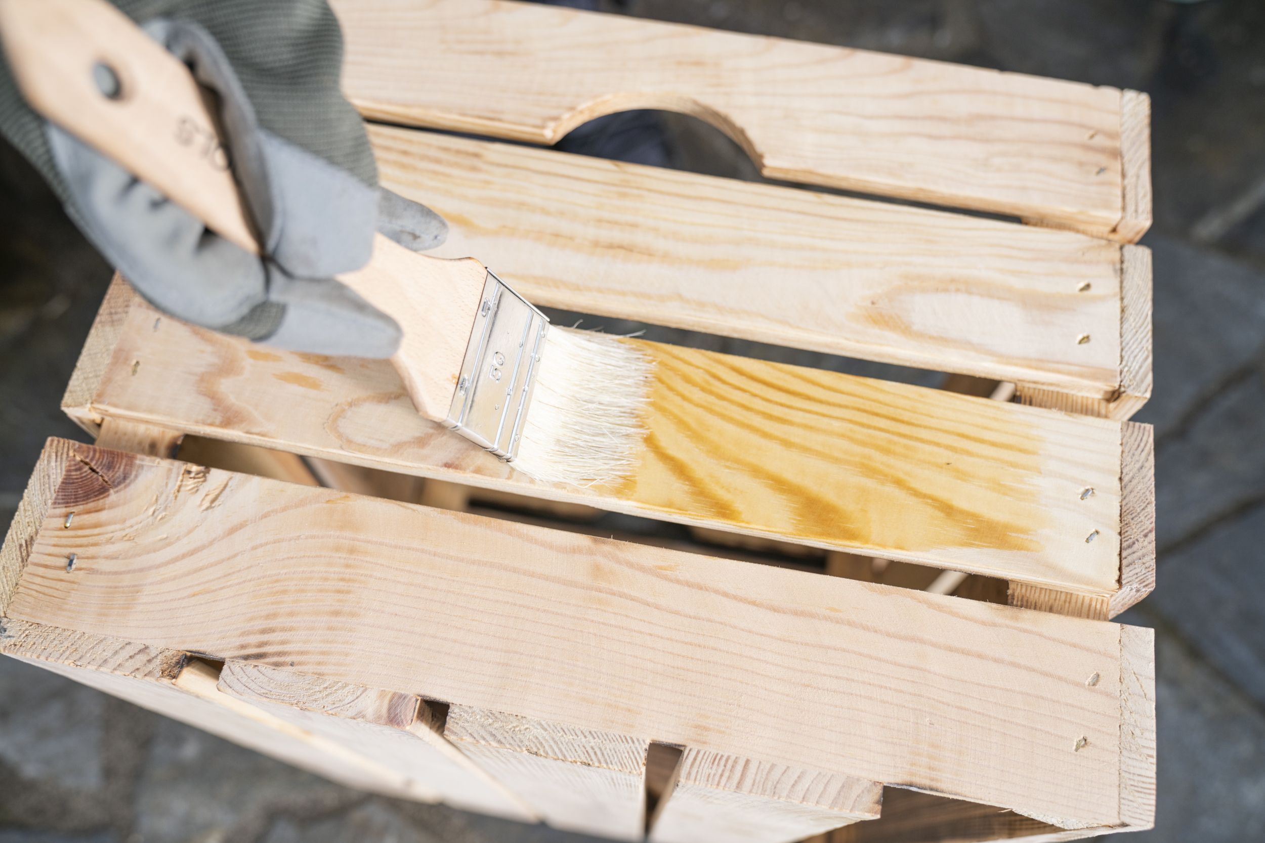 Egy fadobozt faolajjal és ecsettel kezelnek.