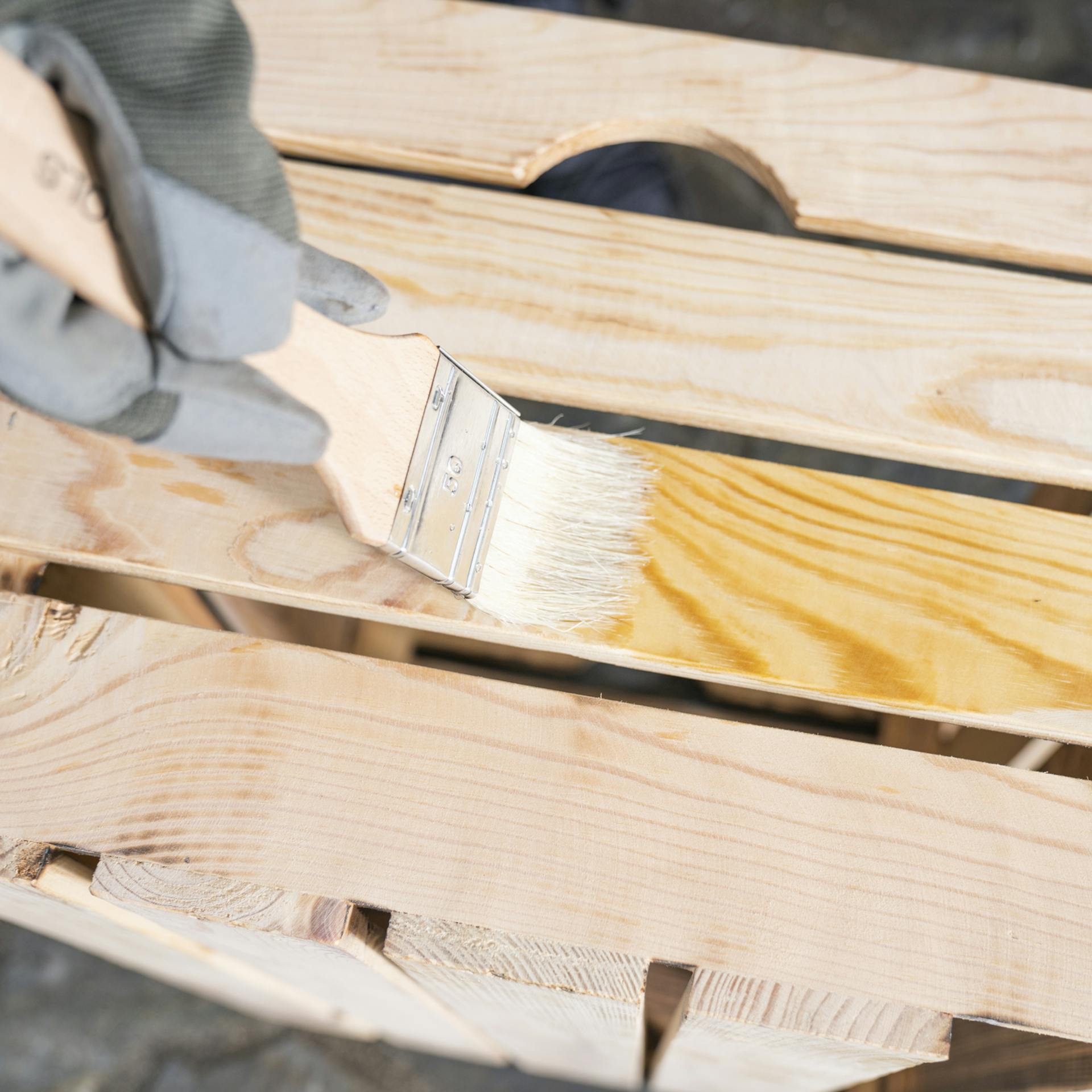 Eine hochkant stehende Holzkiste wird mit Holz-Öl und einem Pinsel behandelt.