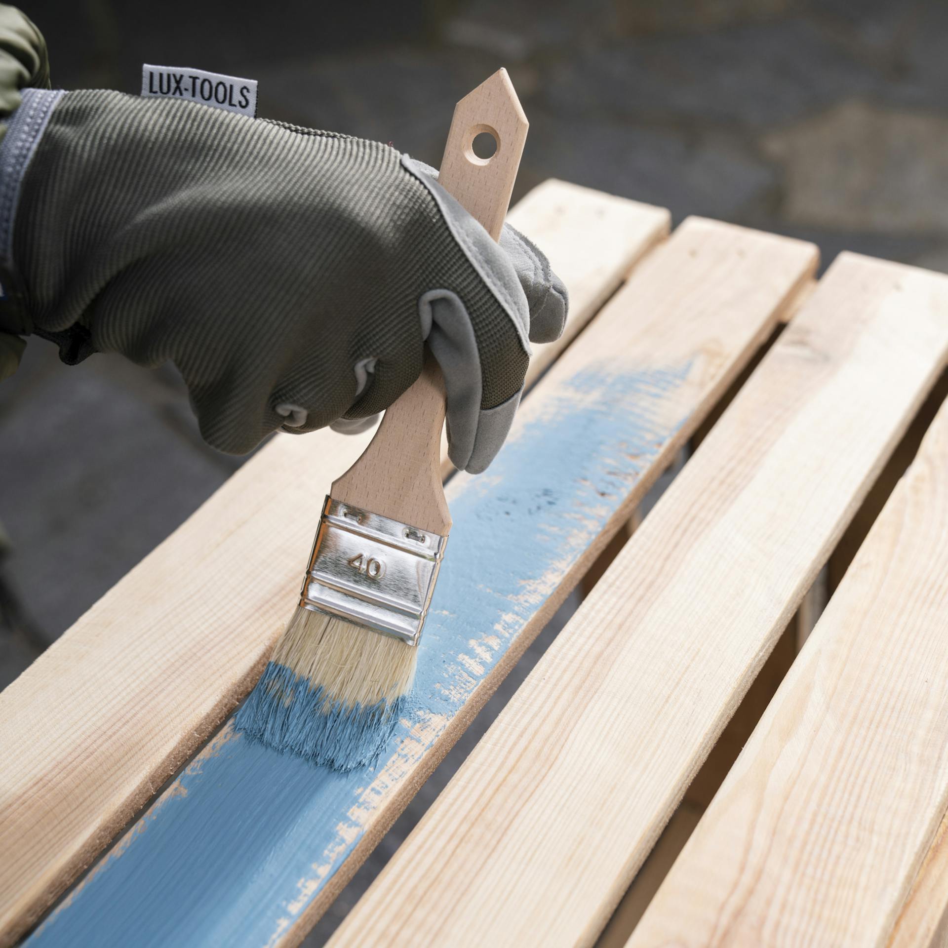 Die lange Seite einer Holzkiste wird mit blauer Farbe gestrichen.