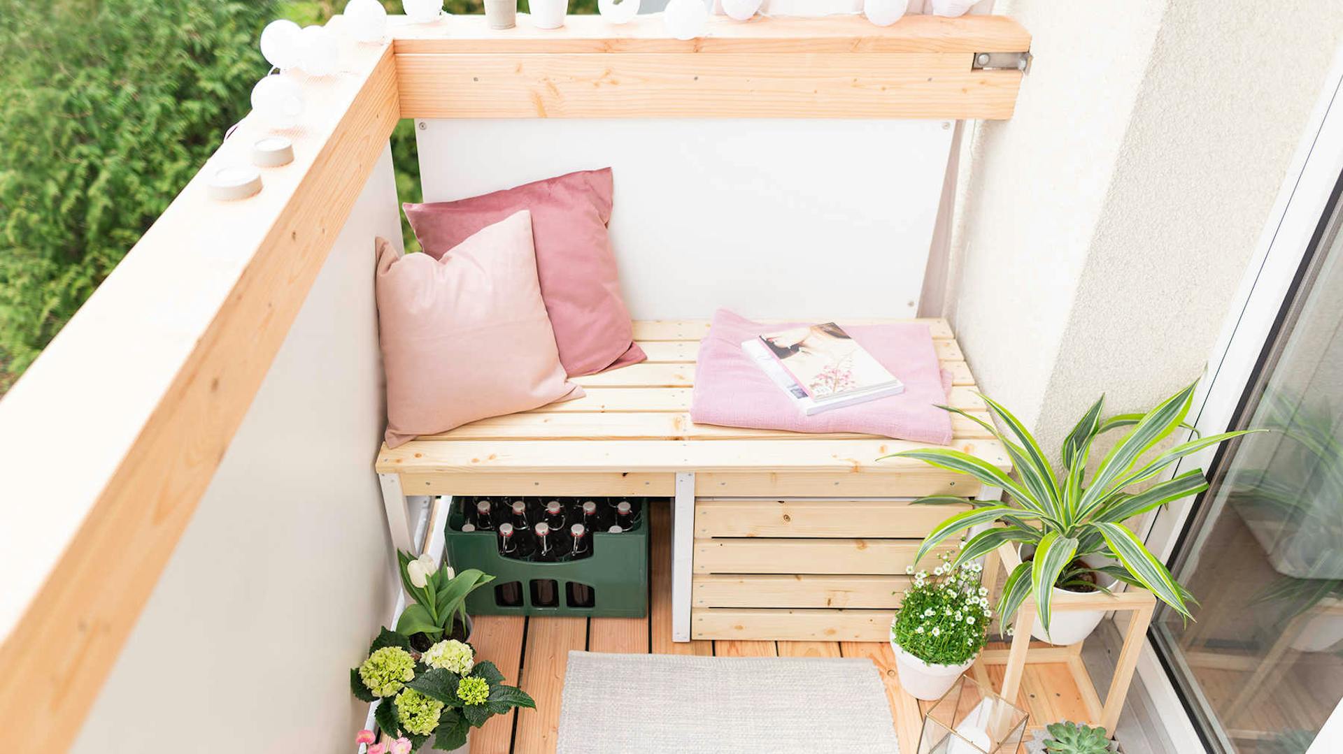 Frontansicht der aus Vollholz bestehenden Balkonbank Lasse in naturfarbe mit viel Stauraum auf einem Balkon.