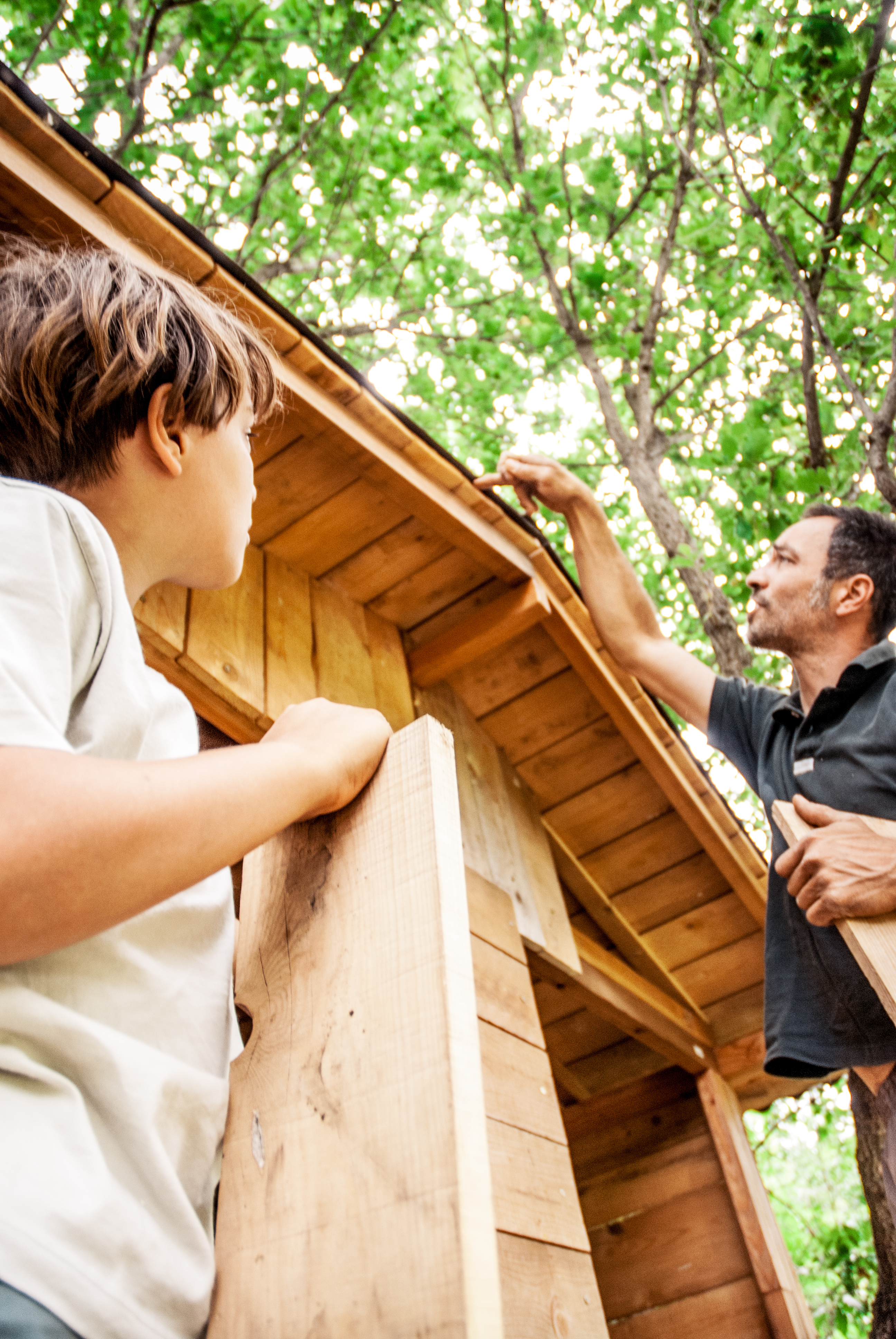Otec kontroluje střechu domku na stromě, zda není poškozená.