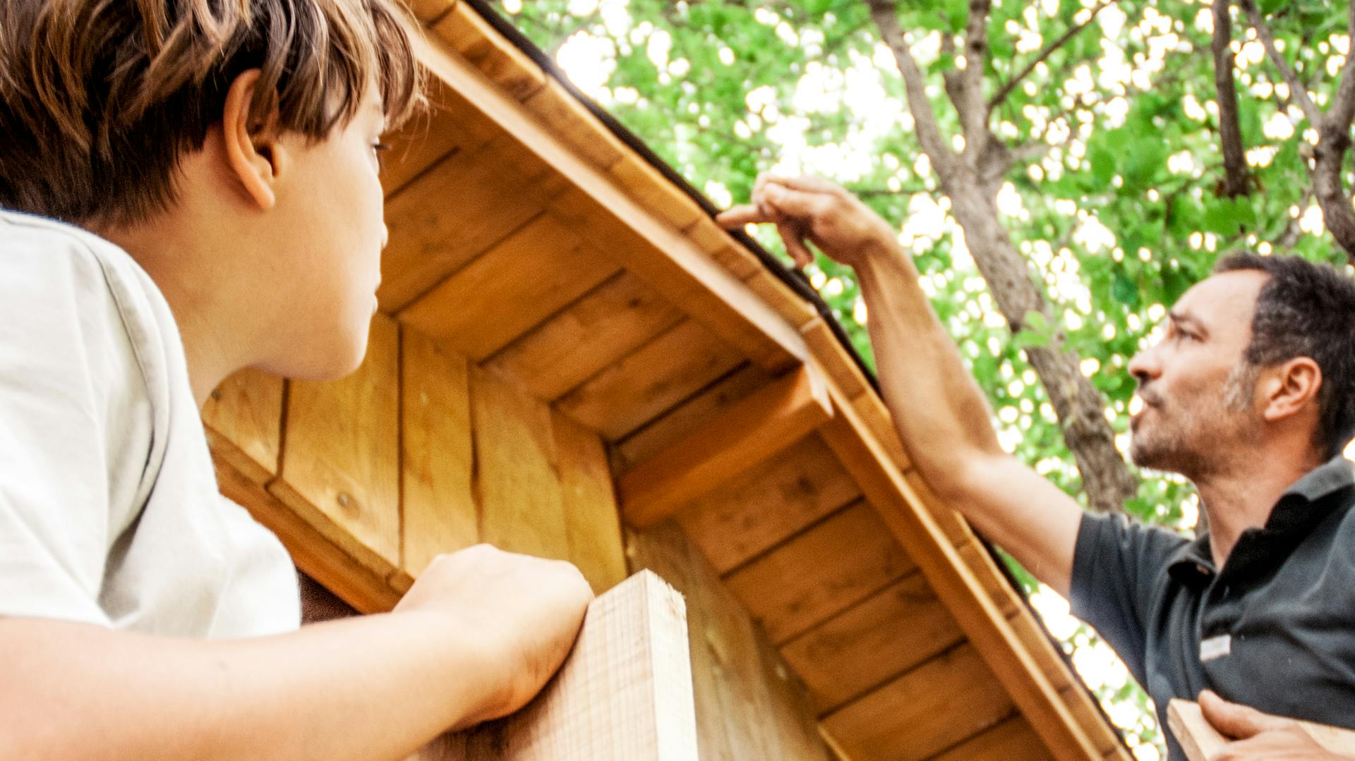 Otec kontroluje střechu domku na stromě, zda není poškozená.