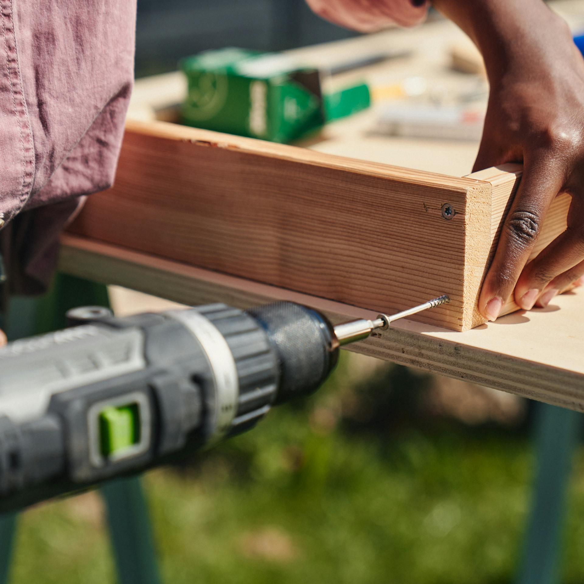 Egy nő deszkákat csavaroz össze egy akkus csavarhúzóval.