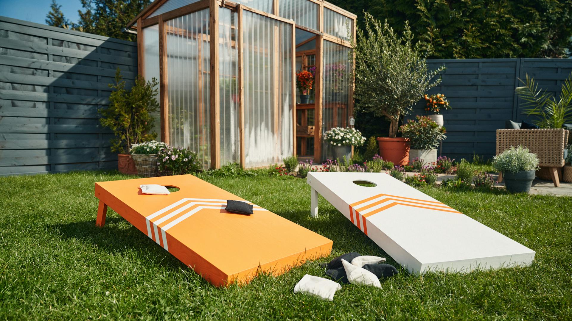 Zwei orange lackiertes Cornholeboards liegen im Gras.