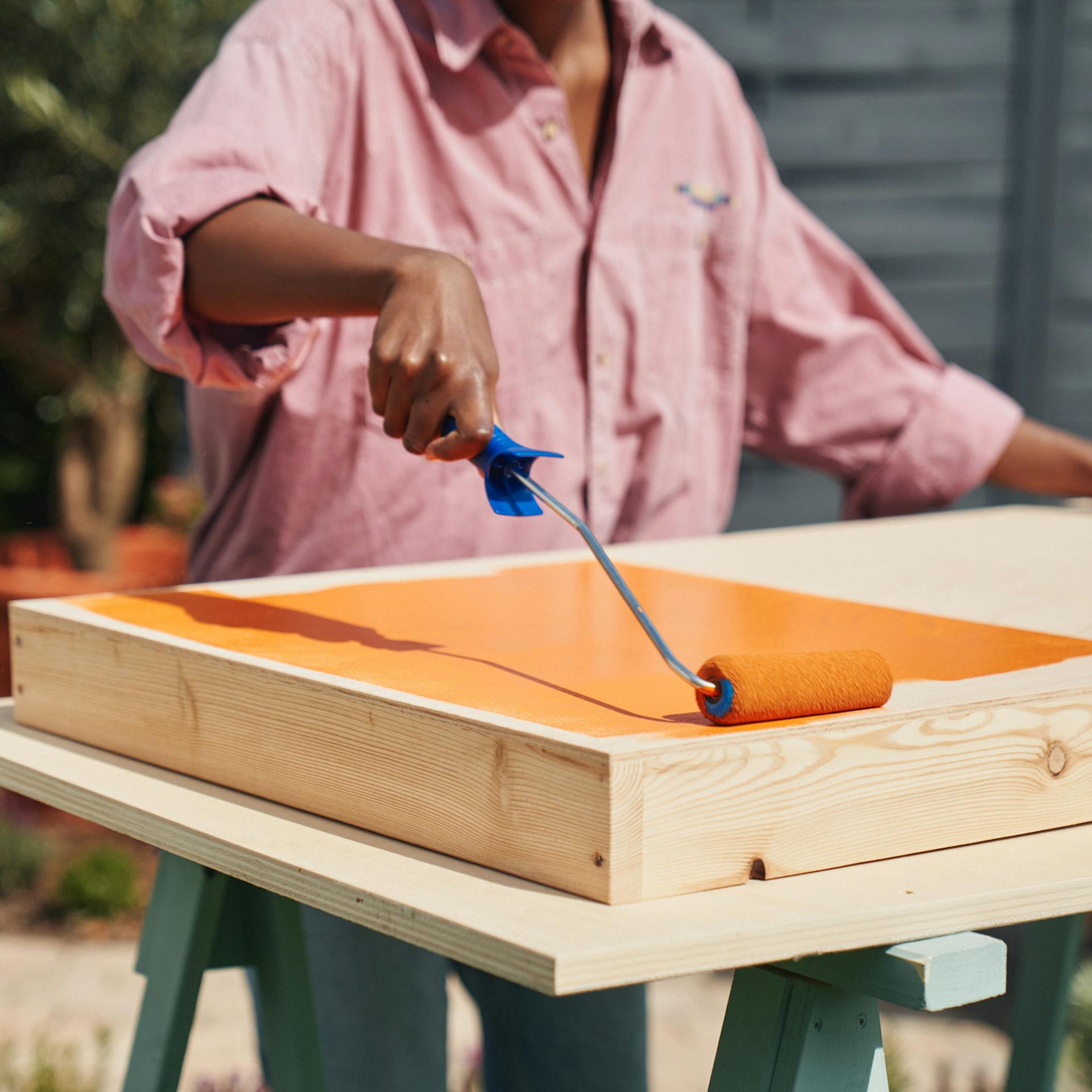 Egy nő festőhengerrel narancssárga festékkel festi a babzsákdobó céltáblát.