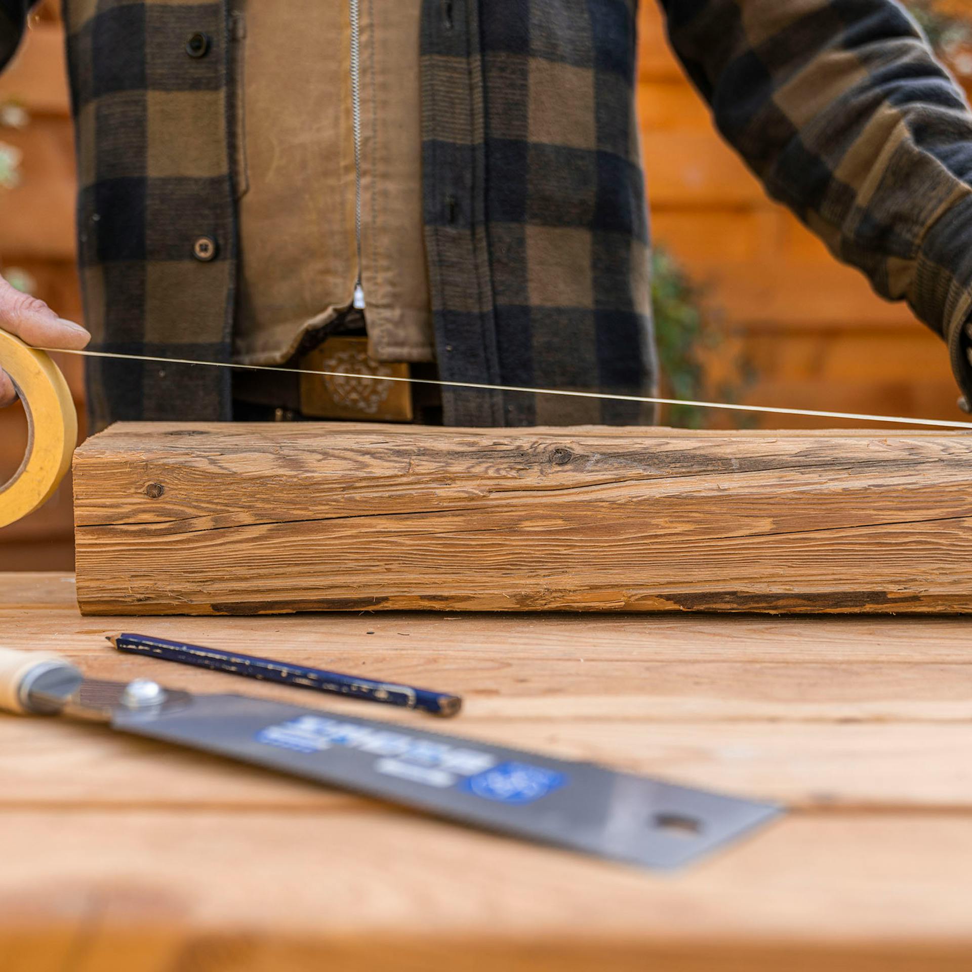 A férfi egy maszkolószalagot ragaszt hosszában a fa egyik oldalára.