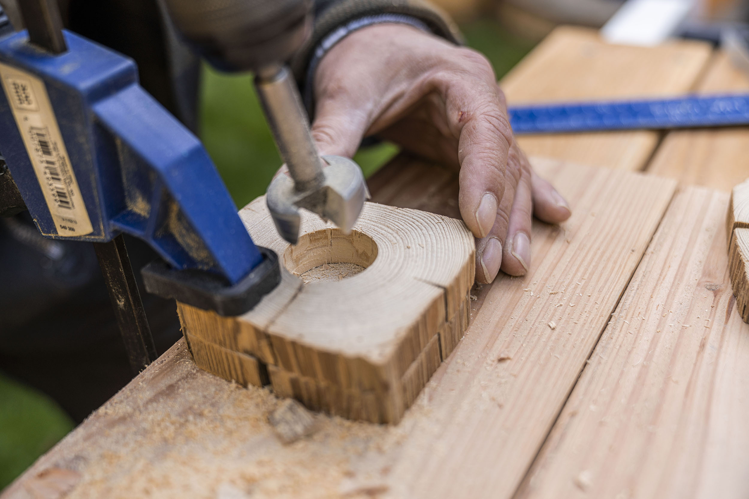 A férfi a sablont és egy másik fakorongot egy egykezes szorítóval rögzíti az asztalhoz.