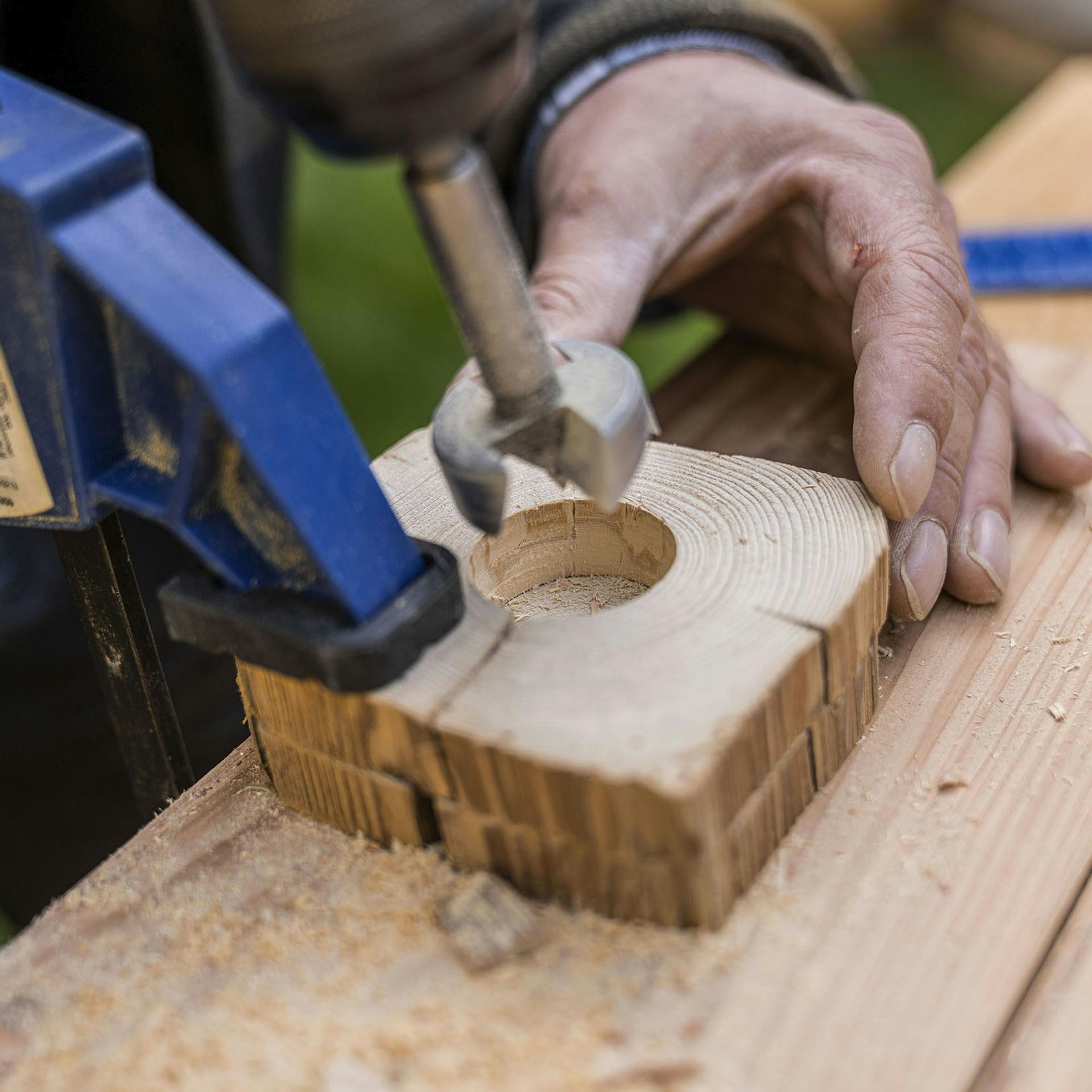 A férfi a sablont és egy másik fakorongot egy egykezes szorítóval rögzíti az asztalhoz.