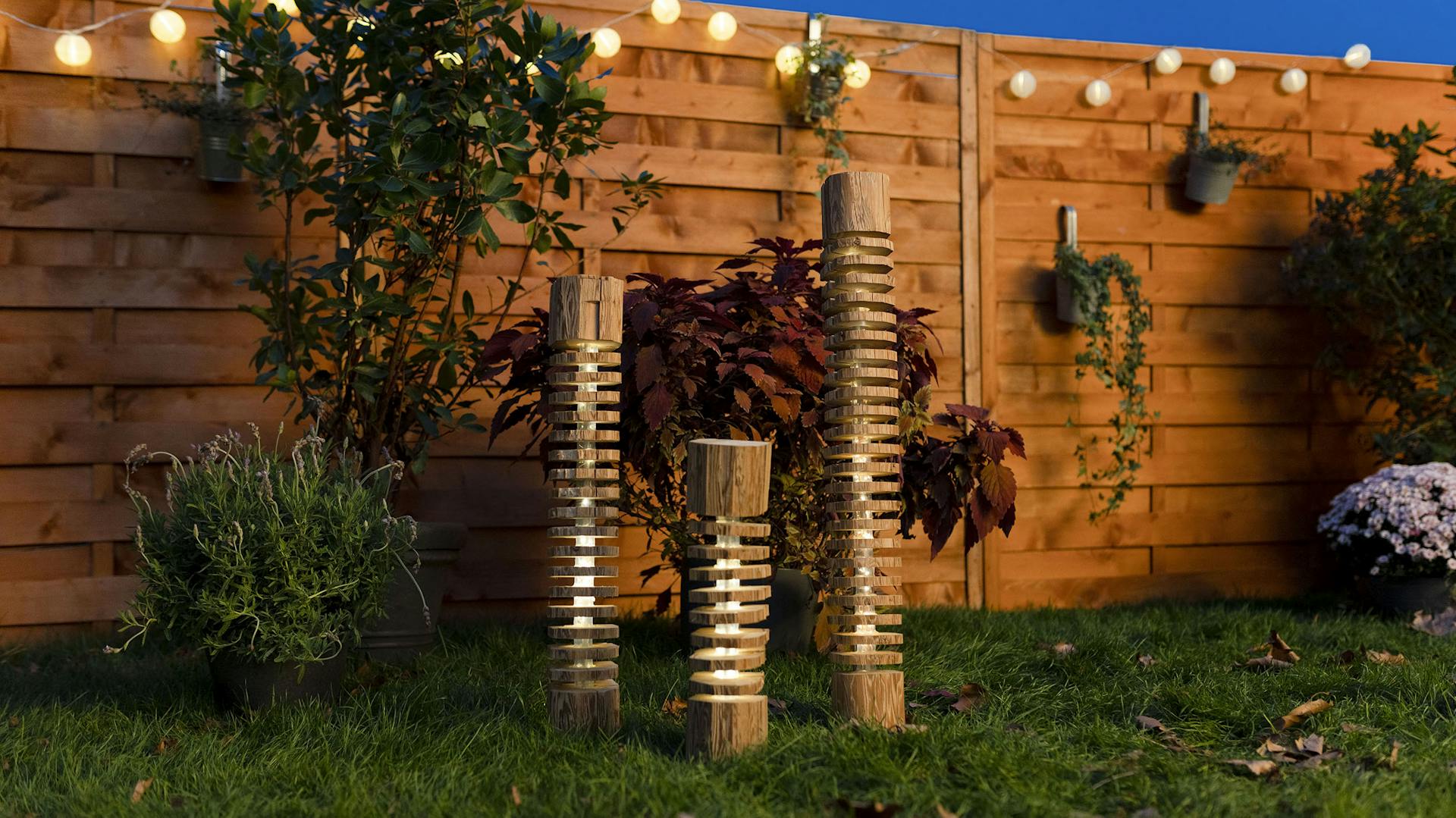 Drei DIY-Hollzlampen stehen nebeneinander im Garten auf einer Wiese.