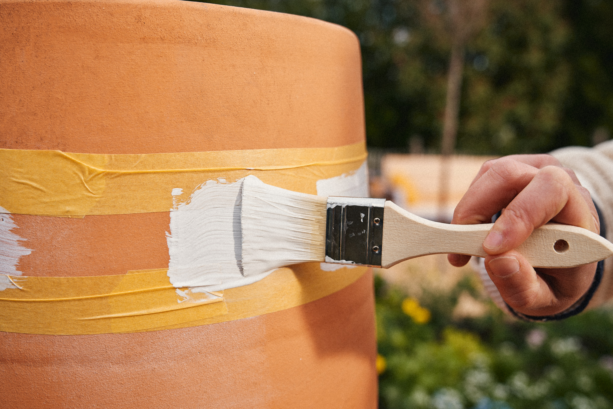 Egy nő festi a terrakotta cserepet fehér festékkel.